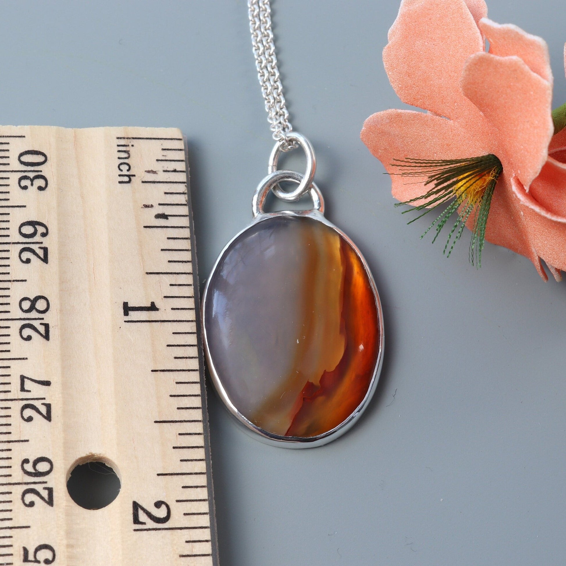 A 1.62 inch Carnelian gemstone was selected for its glassy luster, unique variation of semi-translucent grays and rich deep orange hues. In our Missouri studio, we hand-cut and polished this into a cabochon shape and set in a handcrafted sterling silver Argentium 935 bezel paired with a complementary Argentium silver chain. The Carnelian has been used for centuries in jewelry, amulets and seal making it a timeless and versatile statement piece.