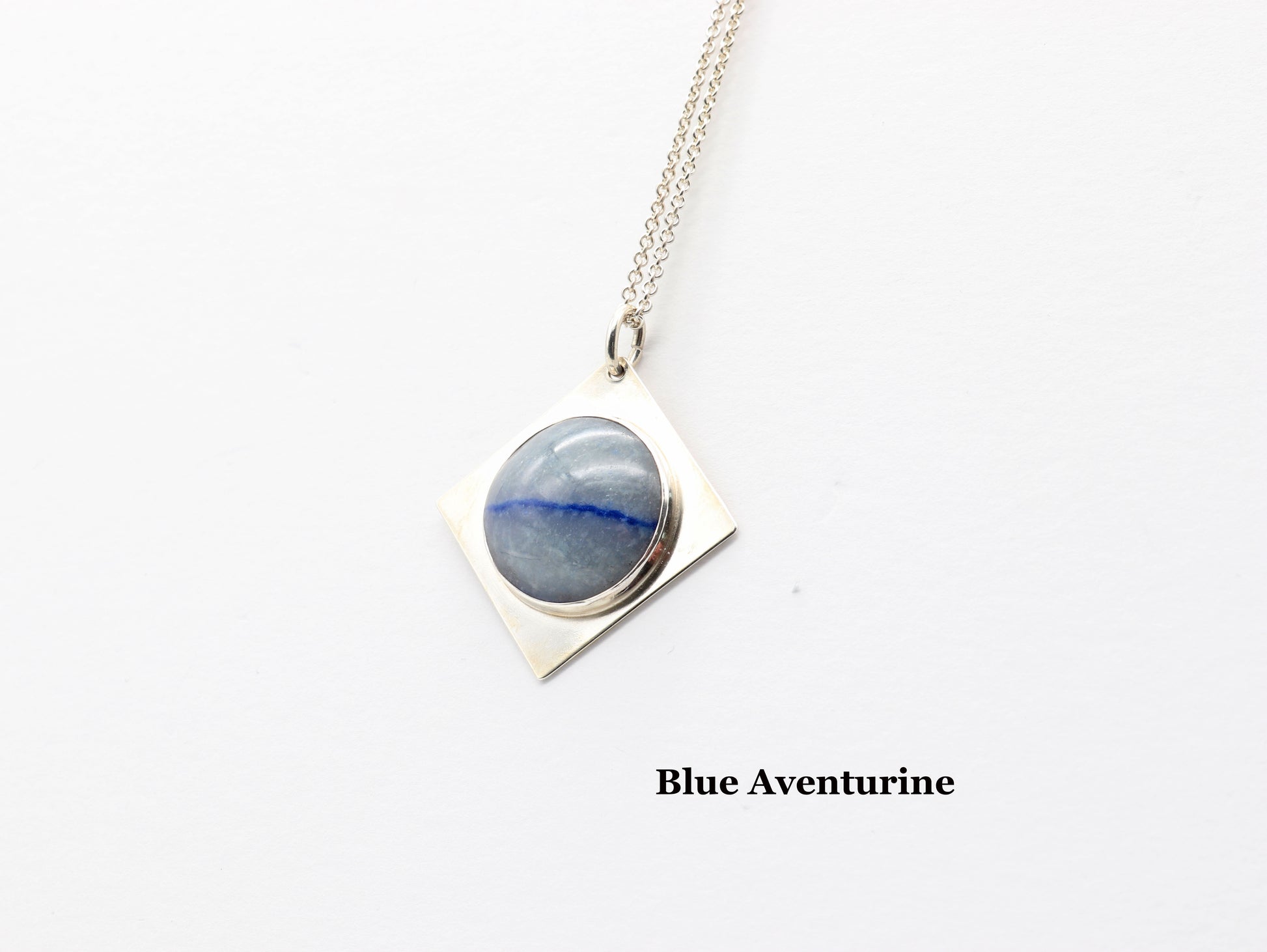A handcut Blue Aventurine cabochon with shimmering crystalline structure and a deep indigo inclusion, reminiscent of Saturn’s rings.  Text overlay is Blue Aventurine