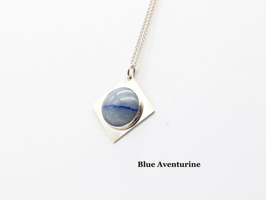 A handcut Blue Aventurine cabochon with shimmering crystalline structure and a deep indigo inclusion, reminiscent of Saturn’s rings.  Text overlay is Blue Aventurine