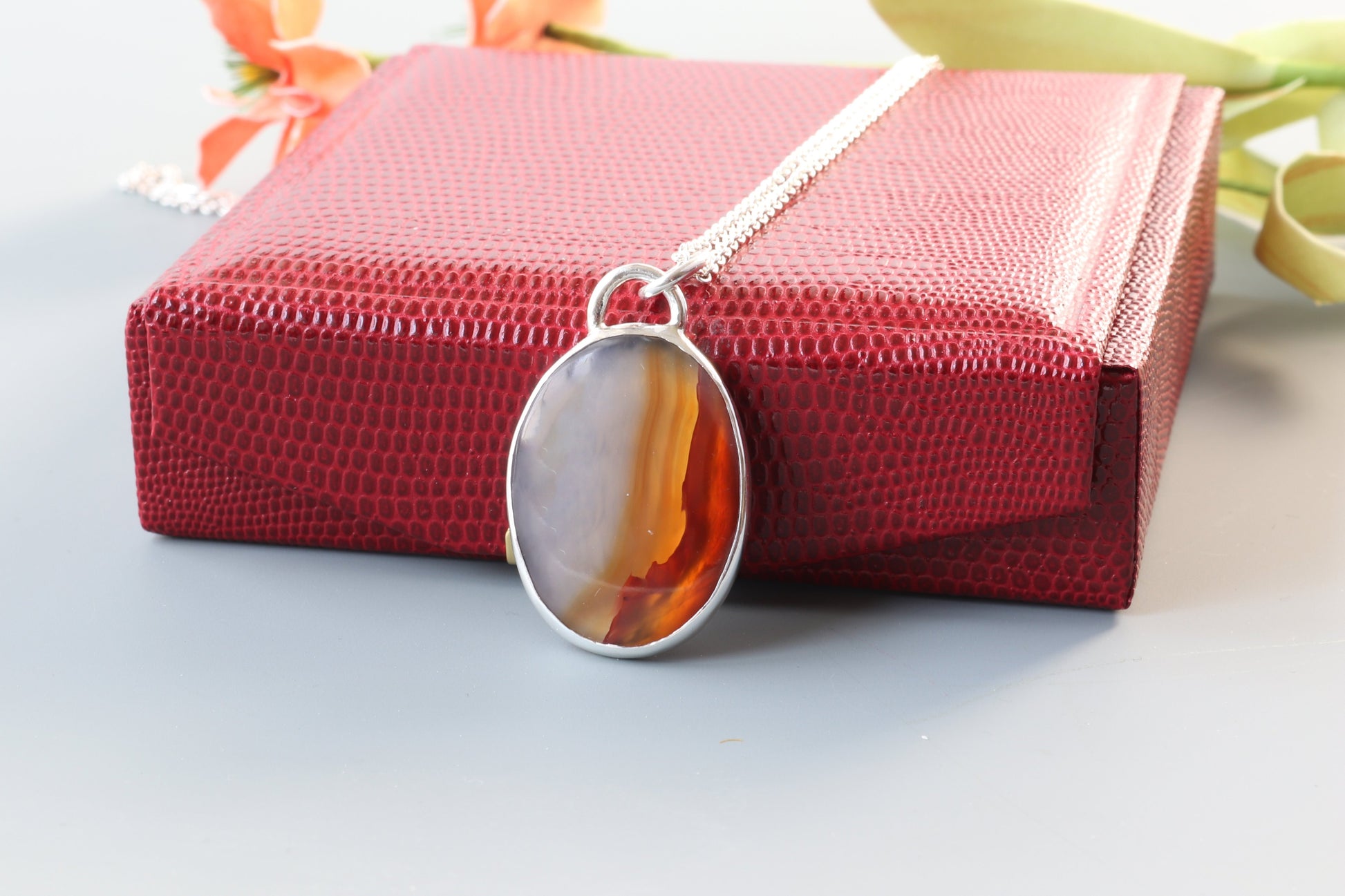 A Carnelian gemstone was selected for its glassy luster, unique variation of semi-translucent grays and rich deep orange hues. In our Missouri studio, we hand-cut and polished this into a cabochon shape and set in a handcrafted sterling silver Argentium 935 bezel paired with a complementary Argentium silver chain. Ready to gift in a red faux leather gift box.
