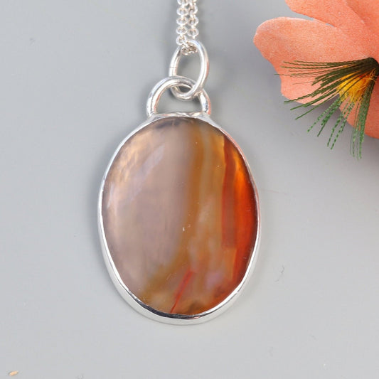A Carnelian gemstone was selected for its glassy luster, unique variation of semi-translucent grays and rich deep orange hues. In our Missouri studio, we hand-cut and polished this into a cabochon shape and set in a handcrafted sterling silver Argentium 935 bezel paired with a complementary Argentium silver chain. The Carnelian has been used for centuries in jewelry, amulets and seal making it a timeless and versatile statement piece.