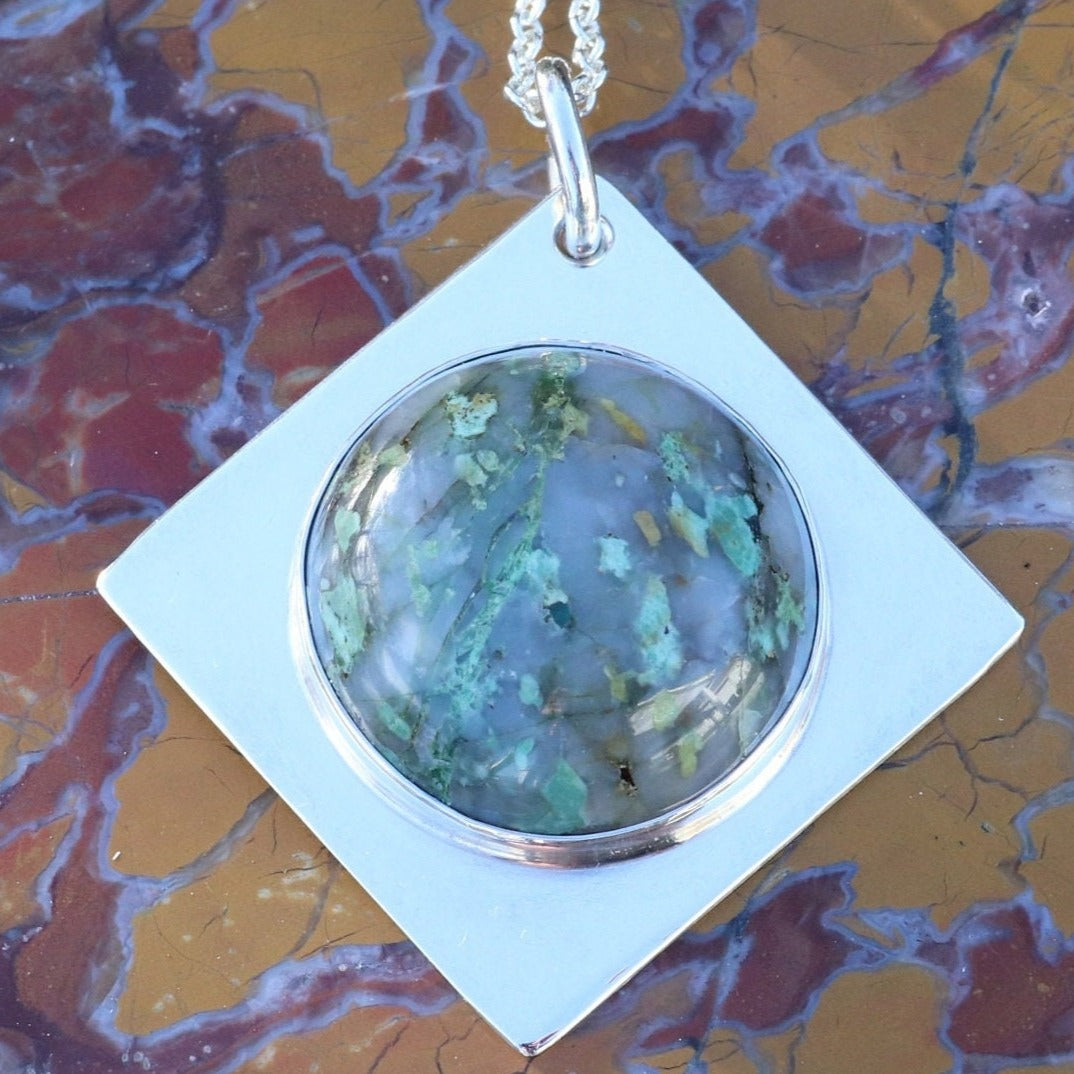 Close-up of Variscite Pendant set in Argentium Silver against red and brown rock background.
