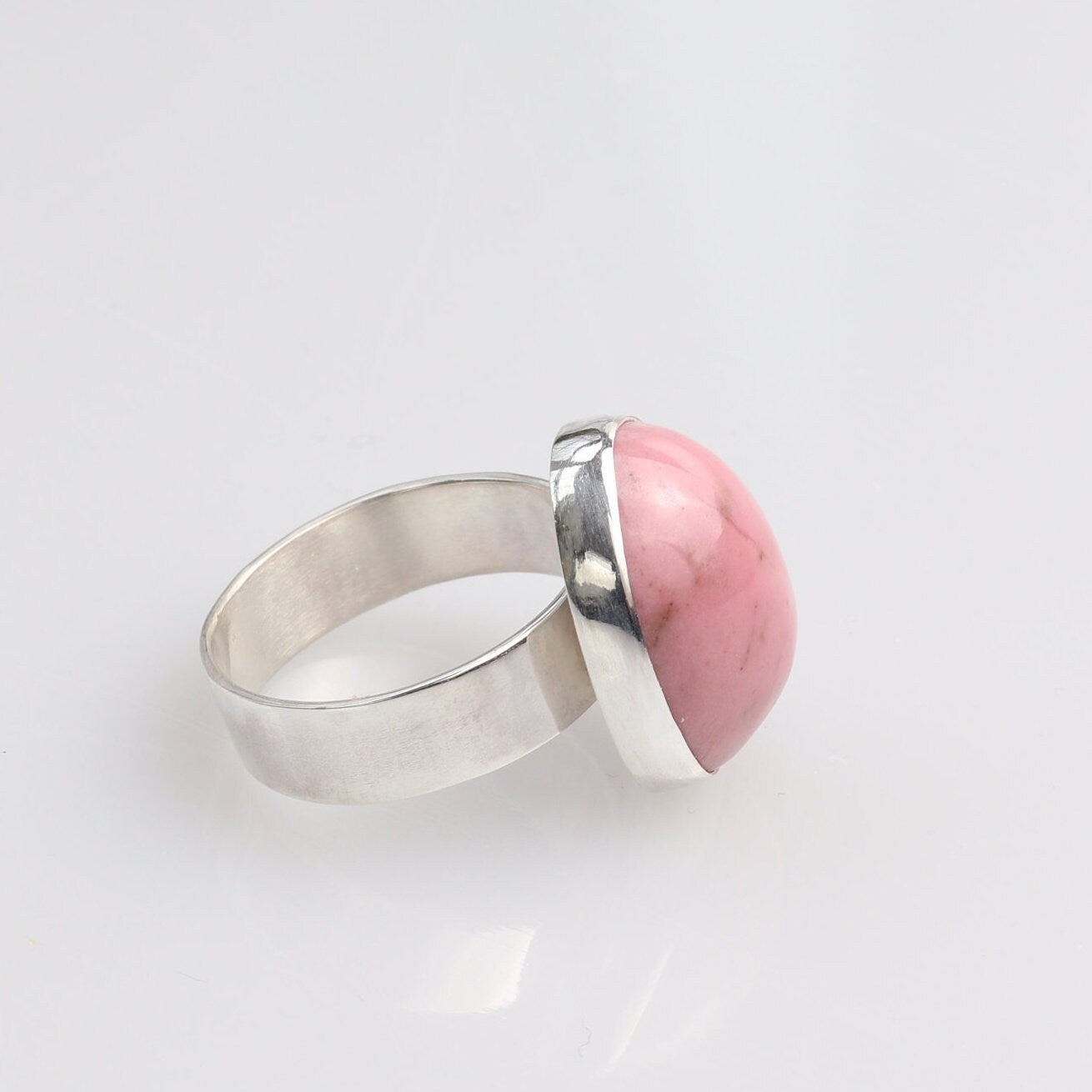 A closeup of side view of  handcrafted pink Rhodonite gemstone ring. The stone has been handcut and polished into a smooth cabochon to reveal its rich rose hue and subtle black veining.