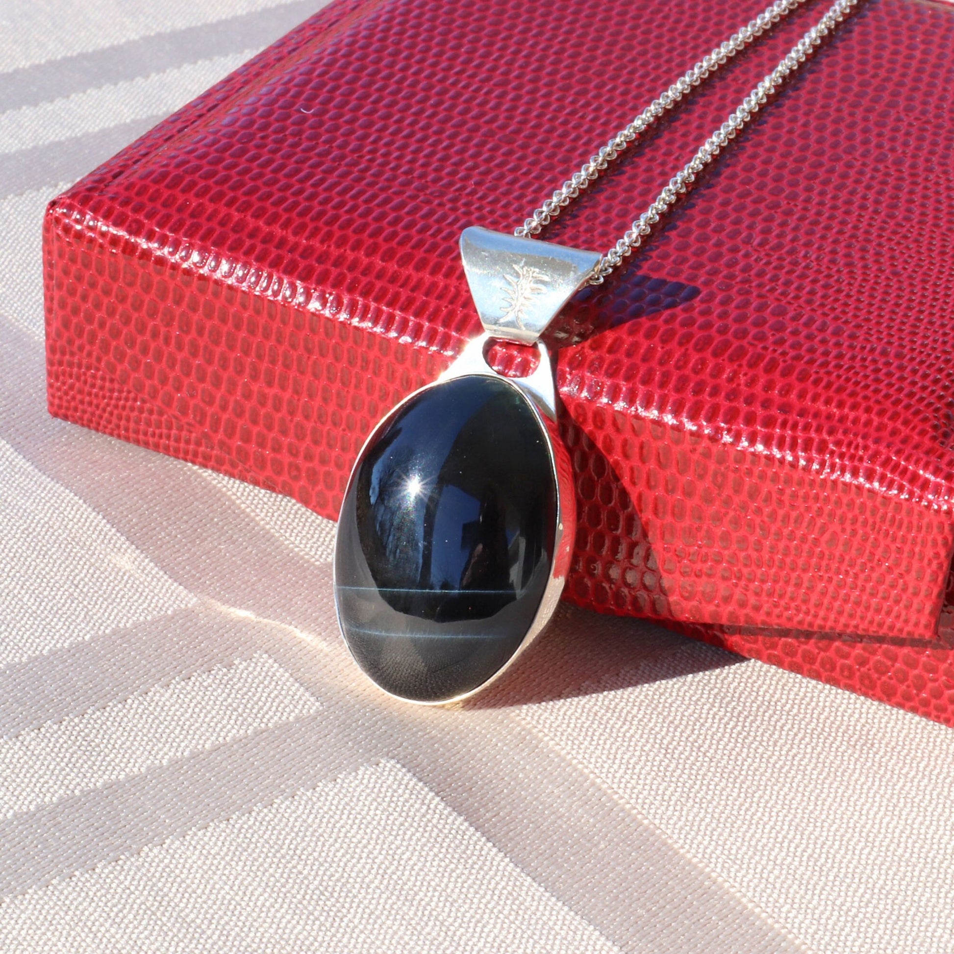 A rare African Blue Tiger's Eye gemstone handcut and polished in our Missouri studio. This one-of-a-kind gem is meticulously fashioned in Argentium 935 Silver  The African Blue Tiger's Eye cabochon with unique coloring and blue striped patterns, making this piece one-of-a-kind.
Ready to gift in a faux red leather gift box.
