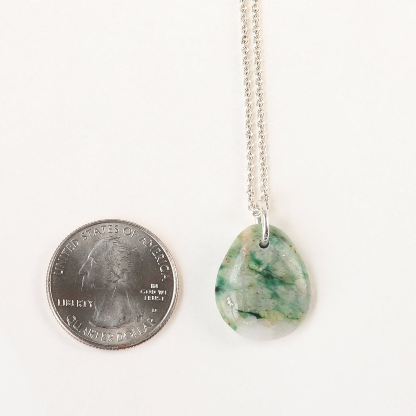 A stunning 24.68 mm Mariposite gemstone pendant, handcrafted in Missouri, USA. This unique piece features a teardrop shape, handcut and polished on both sides to showcase the natural green and white hues of the Mariposite stone. The pendant is complemented by a custom 940 Argentium silver bail, adding a touch of sophistication to the design. To make this piece ready to wear, an optional matching 1.7 Argentium silver chain is offered.
