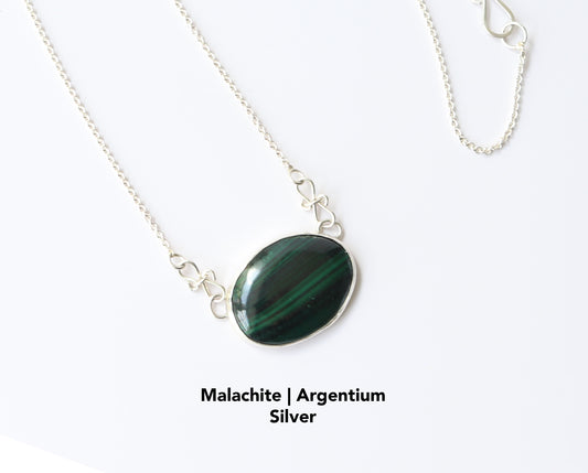 A unique Malachite gemstone pendant hand-cut and polished stone and set in solid sterling 935 Argentium® Silver. Designed with a custom chain and S hook for easy wearability. Shown against a white marble background.