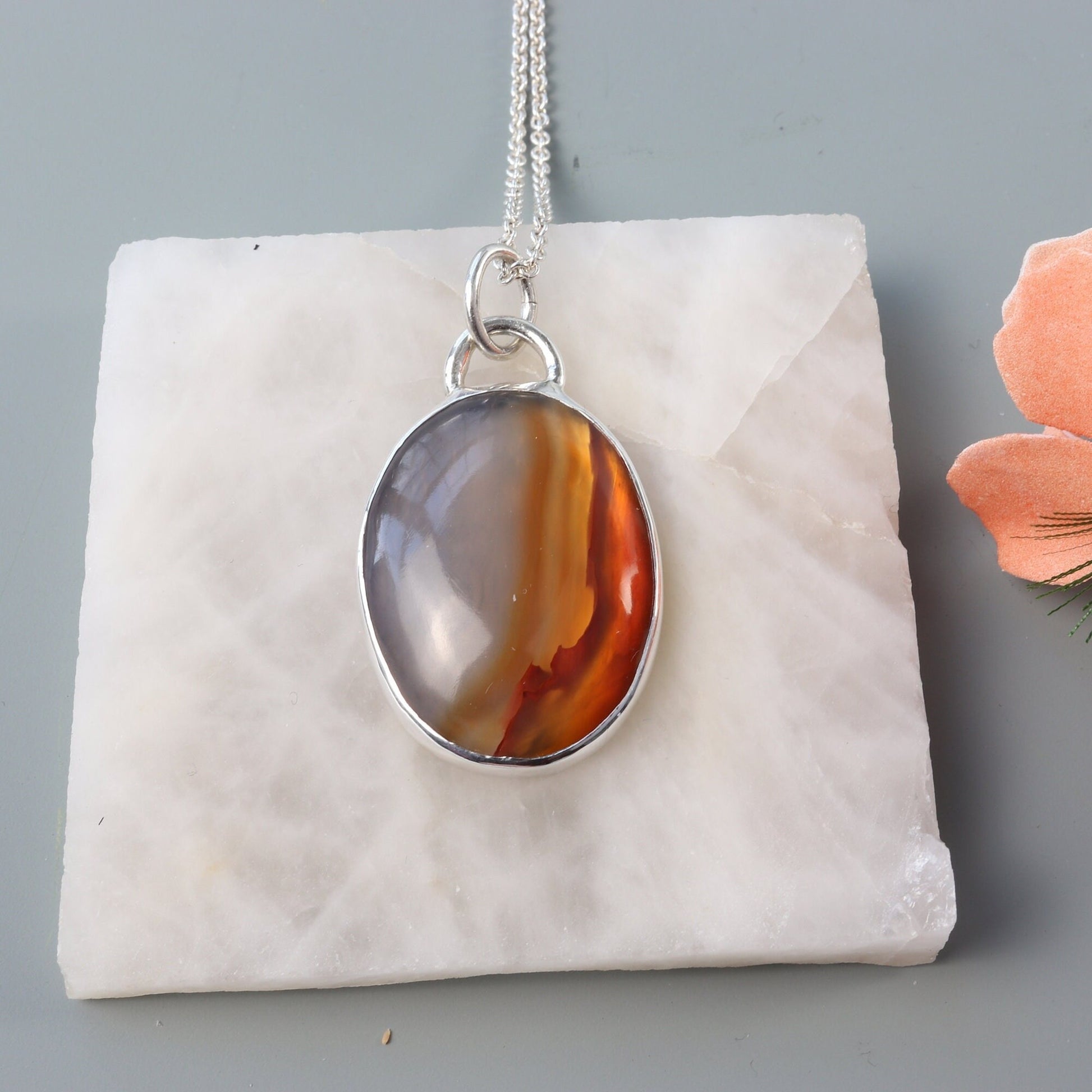 A Carnelian gemstone was selected for its glassy luster, unique variation of semi-translucent grays and rich deep orange hues. In our Missouri studio, we hand-cut and polished this into a cabochon shape and set in a handcrafted sterling silver Argentium 935 bezel paired with a complementary Argentium silver chain. The Carnelian has been used for centuries in jewelry, amulets and seal making it a timeless and versatile statement piece.