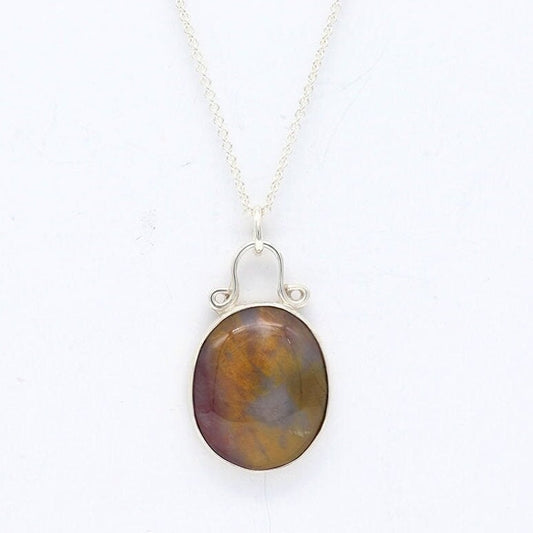 A Petrified Rainbow Wood stone found in Arizona's Petrified Forest, carefully polished by hand in our studio to reveal its stunning charm and vintage appearance. Hanging from a unique and elegant sterling 935 Argentium® Silver bail and setting, this piece is sure to capture your attention and become a cherished part of your jewelry collection.