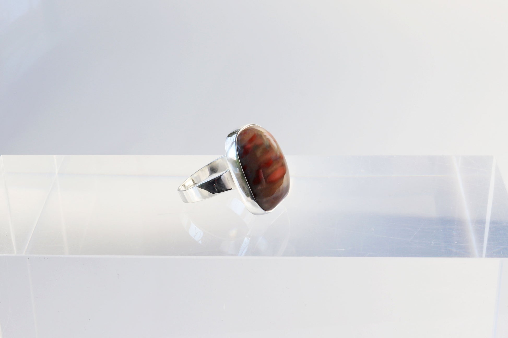A Petrified Rainbow Wood men's gemstone ring.  This gemstone has been handcut and polished in our Missouri studio to showcase the natural red and brown hues and captivating patterns.  Encased in sterling 935 Argentium silver with a fine silver bezel (.999) which work together to create a bold and timeless eye-catching design.