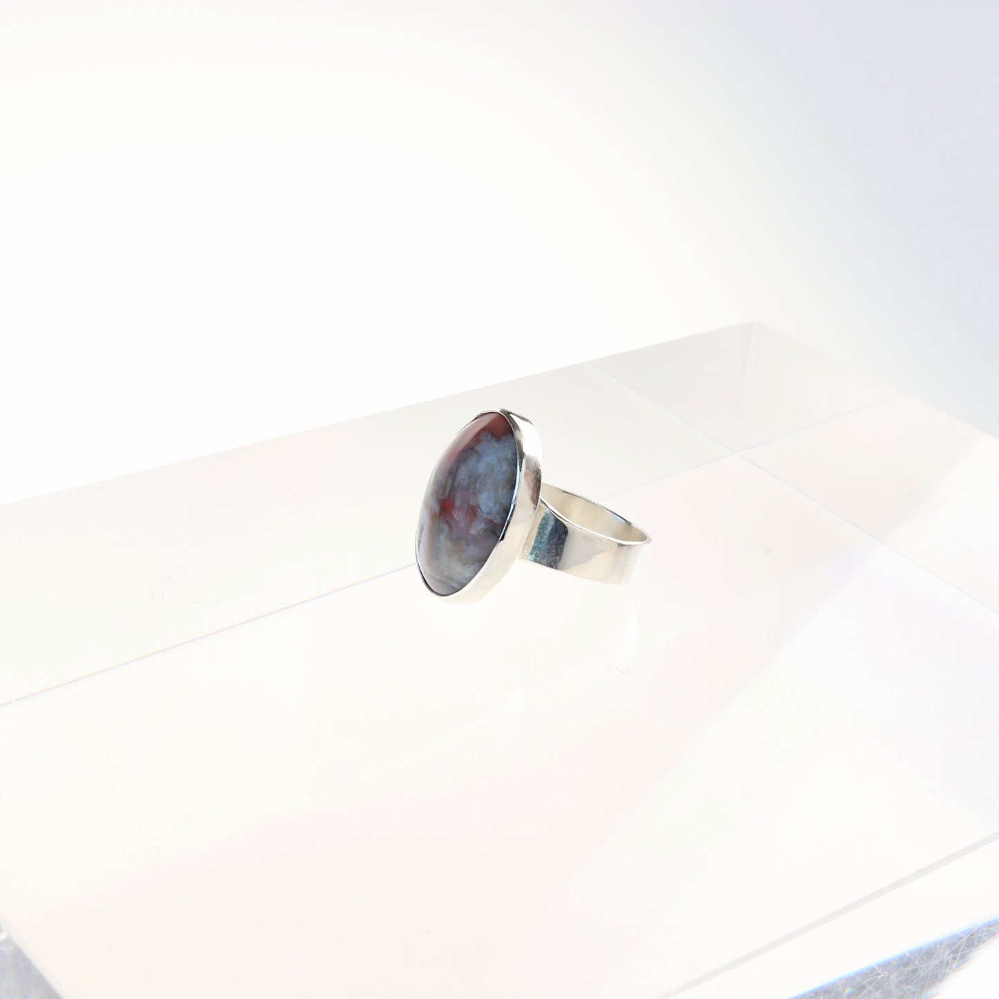 A Crazy Lace Agate Natural Cabochon Gemstone Ring. Handcrafted to reveal the unique swirling patterns and vibrant hues of pink and gray and a unique Crystal feature within the stone. Encased in sterling 935 Argentium silver with a fine silver bezel.