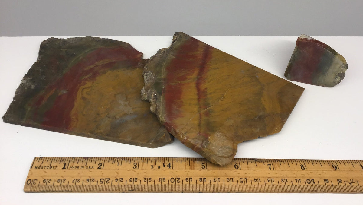 Three rough natural stone slabs of Sonoran Sunrise rocks, displayed on a white surface with a wooden ruler below for scale against a light gray background.