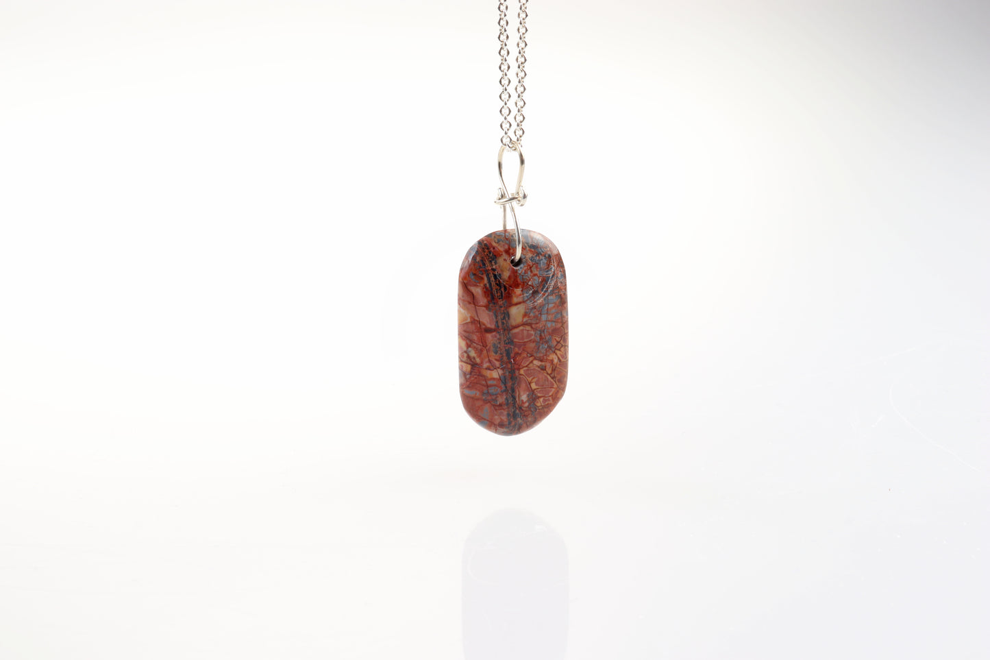 A Stony Creek Jasper gemstone pendant. Handcut and polished on both sides to showcase the unique red and blue patterns of the stone.  The pendant is designed with an original infinity bow shaped wire bail made from Argentium® 935 Silver that is tarnish resistance and has a remarkable shine.  To complete the look a complementary 935 Argentium® silver chain is included.