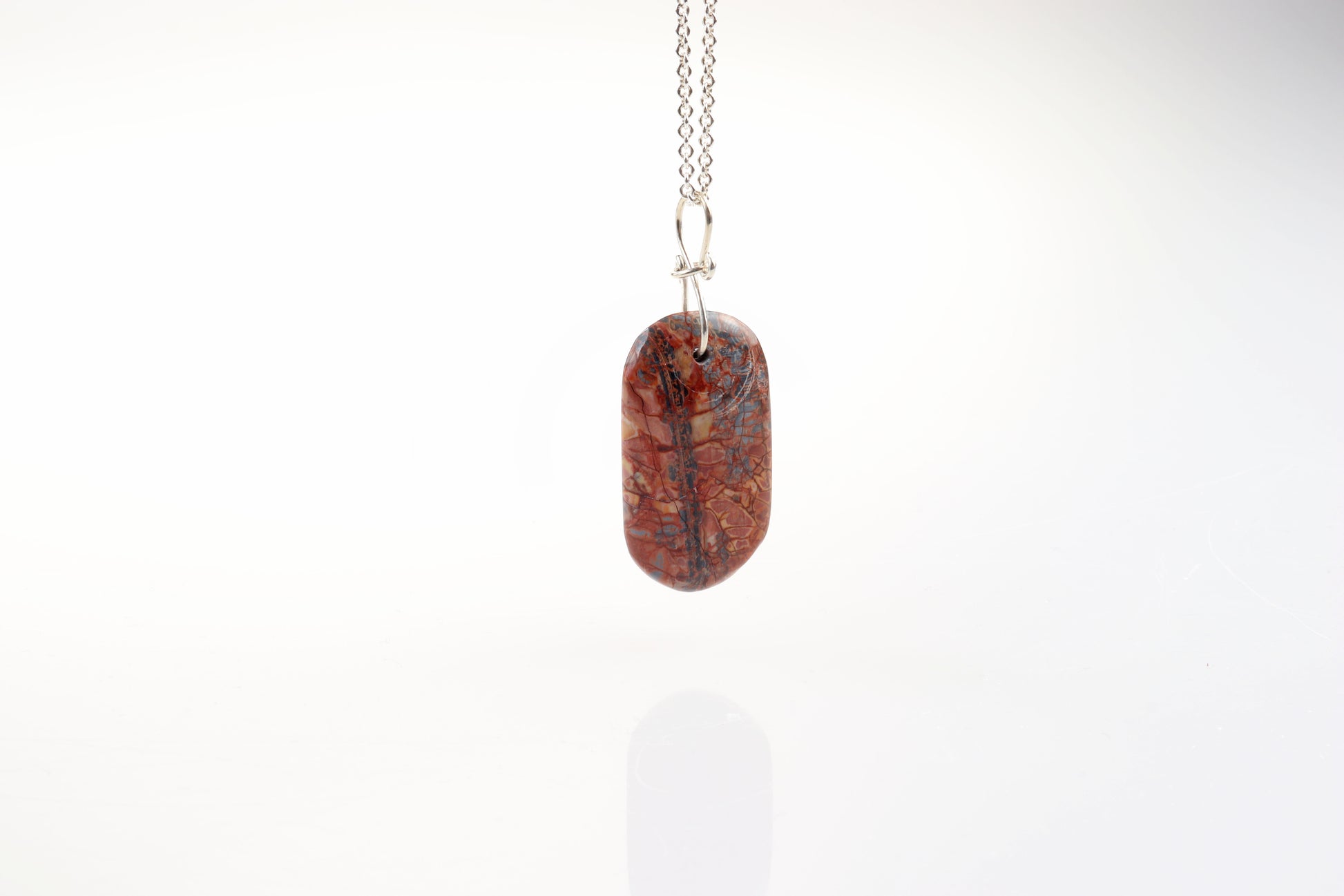 A Stony Creek Jasper gemstone pendant. Handcut and polished on both sides to showcase the unique red and blue patterns of the stone.  The pendant is designed with an original infinity bow shaped wire bail made from Argentium® 935 Silver that is tarnish resistance and has a remarkable shine.  To complete the look a complementary 935 Argentium® silver chain is included.
