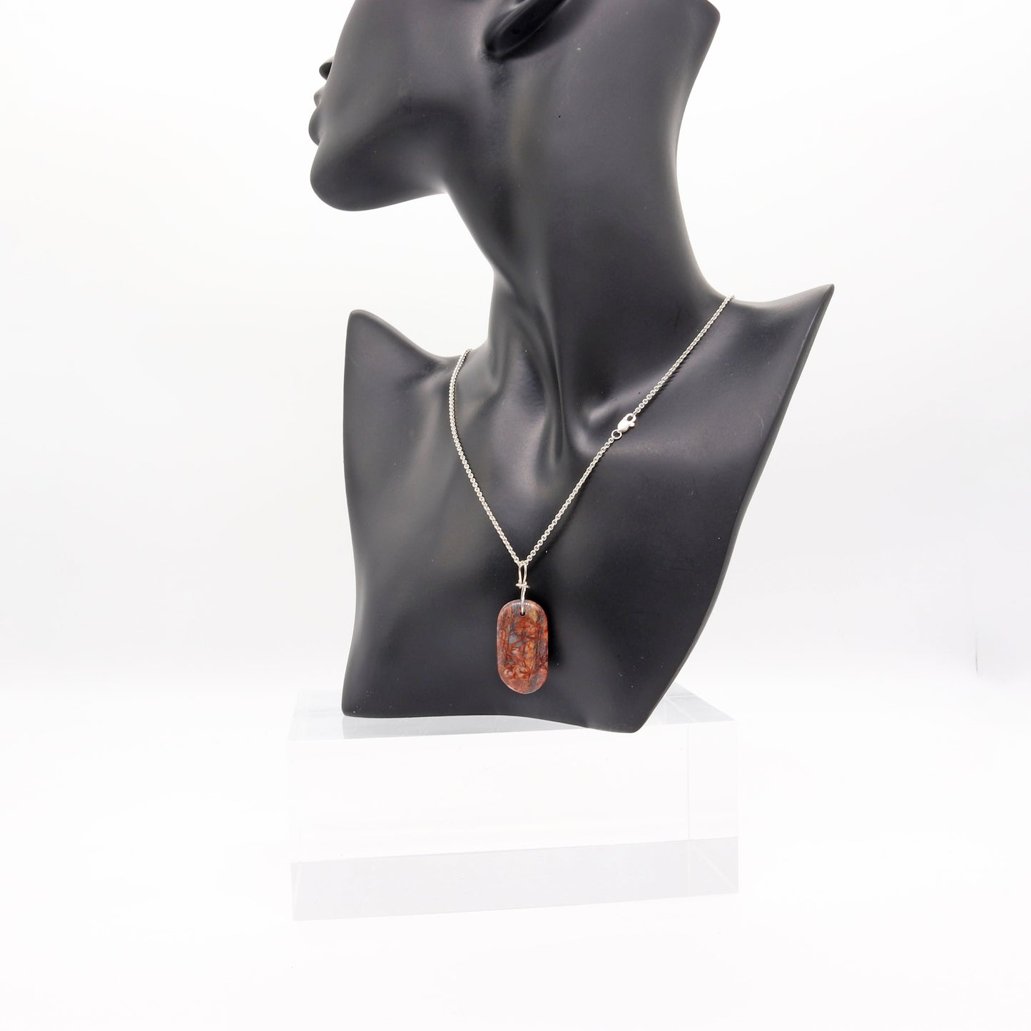A Stony Creek Jasper gemstone pendant. Handcut and polished on both sides to showcase the unique red and blue patterns of the stone.  The pendant is designed with an original infinity bow shaped wire bail made from Argentium® 935 Silver that is tarnish resistance and has a remarkable shine.  To complete the look a complementary 935 Argentium® silver chain is included.