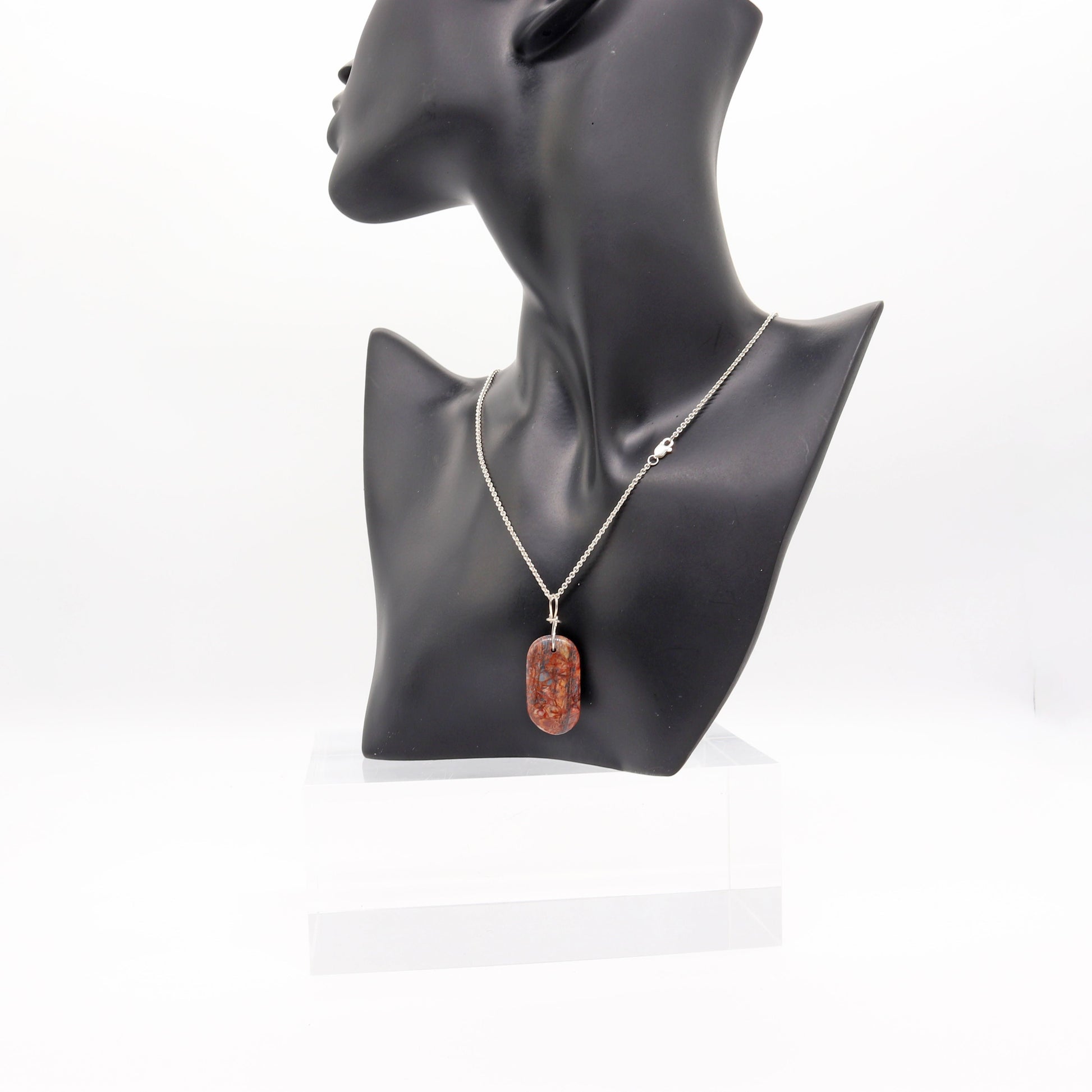A Stony Creek Jasper gemstone pendant. Handcut and polished on both sides to showcase the unique red and blue patterns of the stone.  The pendant is designed with an original infinity bow shaped wire bail made from Argentium® 935 Silver that is tarnish resistance and has a remarkable shine.  To complete the look a complementary 935 Argentium® silver chain is included.