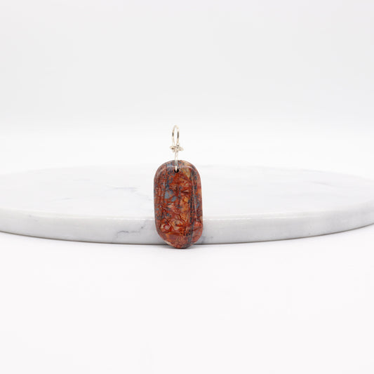 A Stony Creek Jasper gemstone pendant. Handcut and polished on both sides to showcase the unique red and blue patterns of the stone.  The pendant is designed with an original infinity bow shaped wire bail made from Argentium® 935 Silver that is tarnish resistance and has a remarkable shine.  To complete the look a complementary 935 Argentium® silver chain is included.