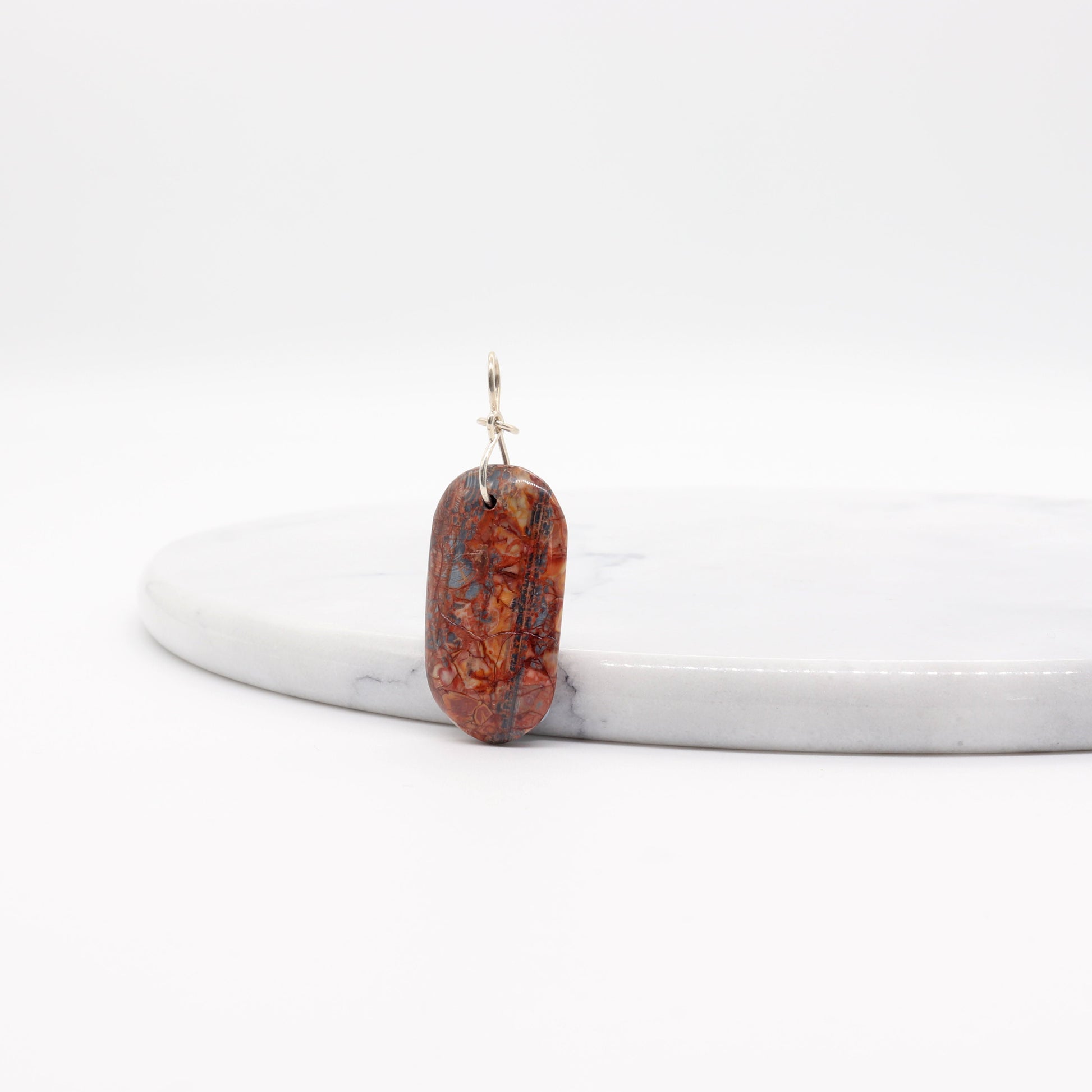 A Stony Creek Jasper gemstone pendant. Handcut and polished on both sides to showcase the unique red and blue patterns of the stone.  The pendant is designed with an original infinity bow shaped wire bail made from Argentium® 935 Silver that is tarnish resistance and has a remarkable shine.  To complete the look a complementary 935 Argentium® silver chain is included.