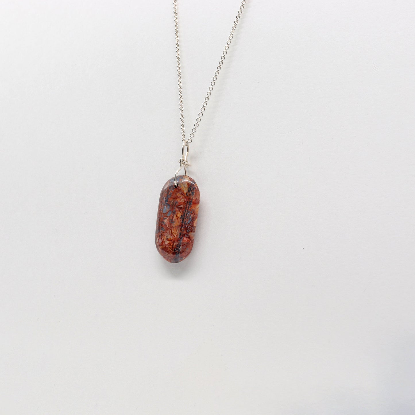 A Stony Creek Jasper gemstone pendant. Handcut and polished on both sides to showcase the unique red and blue patterns of the stone.  The pendant is designed with an original infinity bow shaped wire bail made from Argentium® 935 Silver that is tarnish resistance and has a remarkable shine.  To complete the look a complementary 935 Argentium® silver chain is included.