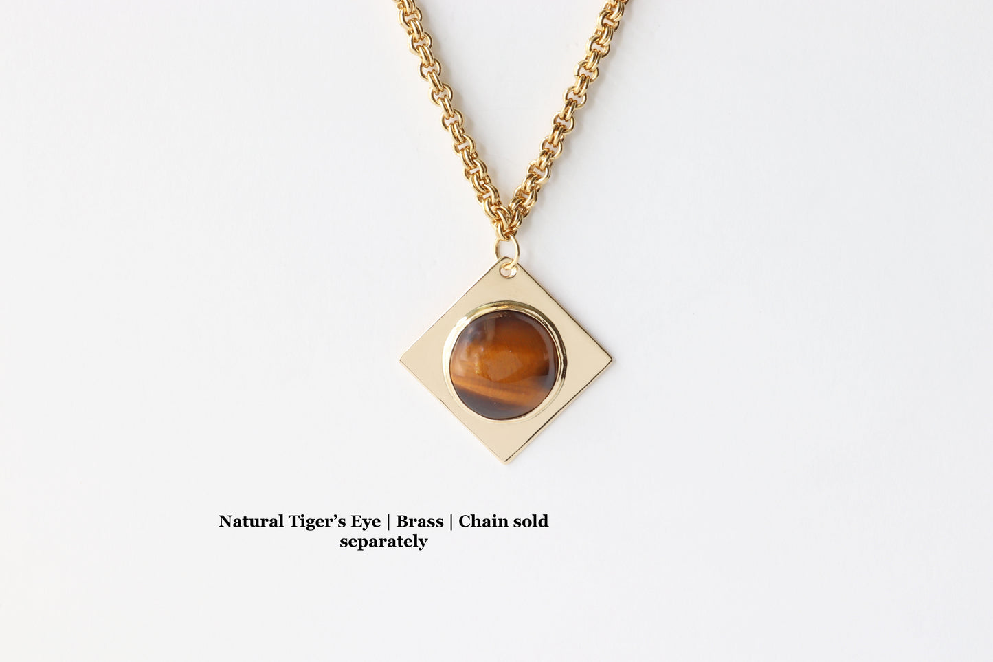 Closeup of a 1.625 Tiger’s Eye pendant, featuring a .75” round cabochon set in a four-point diamond-shaped NuGold brass setting. This one-of-a-kind artisan pendant is hand-cut and polished in our Missouri studio, ensuring a high-quality, handcrafted component for your custom jewelry designs. Shown against white background with double-link brass chain sold separately.