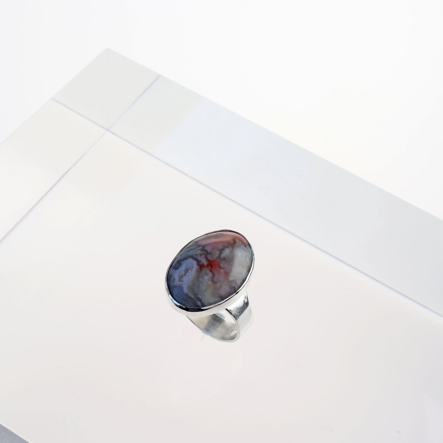A top angled view of this natural Crazy Lace Agate Natural Cabochon Gemstone Ring. Featuring swirling patterns and vibrant hues of pink and gray and a unique Crystal feature within the stone. Encased in sterling 935 Argentium silver with a fine silver bezel.