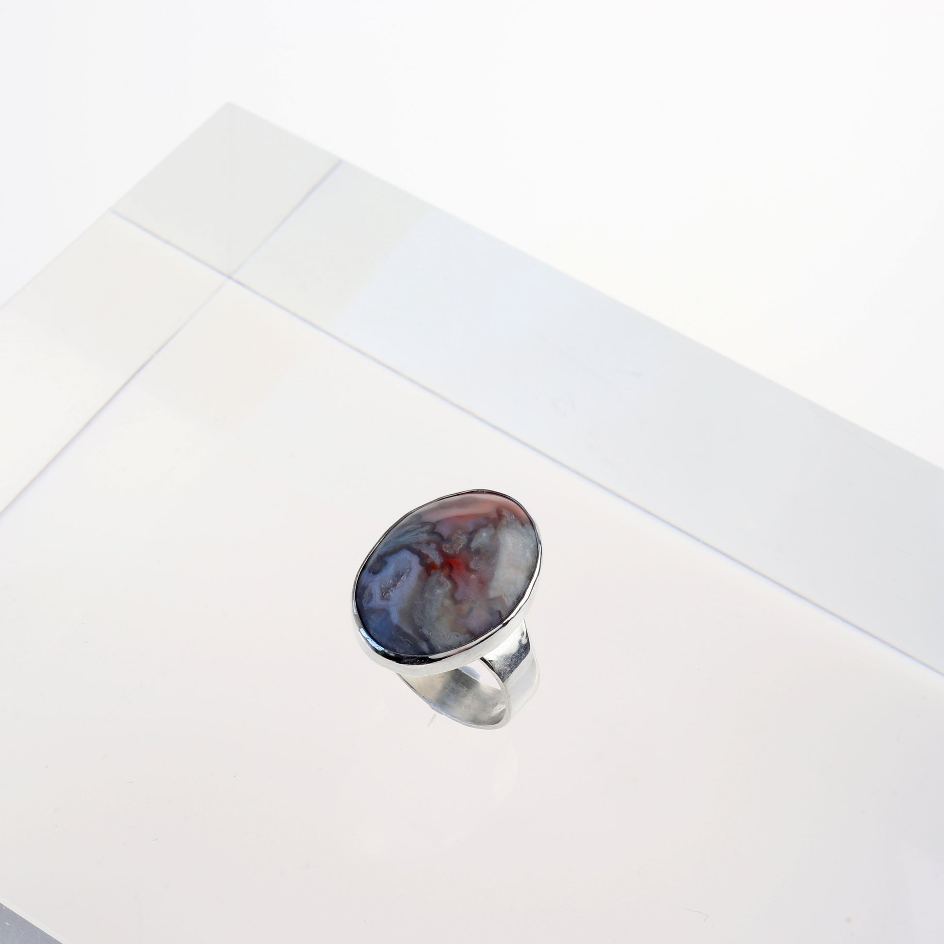 A top angled view of this natural Crazy Lace Agate Natural Cabochon Gemstone Ring.  Featuring swirling patterns and vibrant hues of pink and gray and a unique Crystal feature within the stone. Encased in sterling 935 Argentium silver with a fine silver bezel.