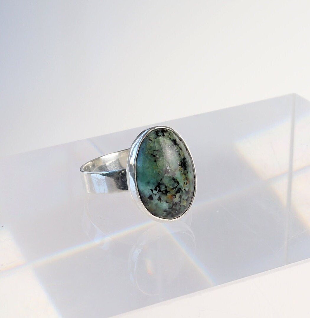 A angle view of Fraser River Turquoise ring features a handcut and polished gemstone with stunning blue-green hues and bold black mottled matrix, echoing the rugged landscape of the Fraser River region in British Columbia