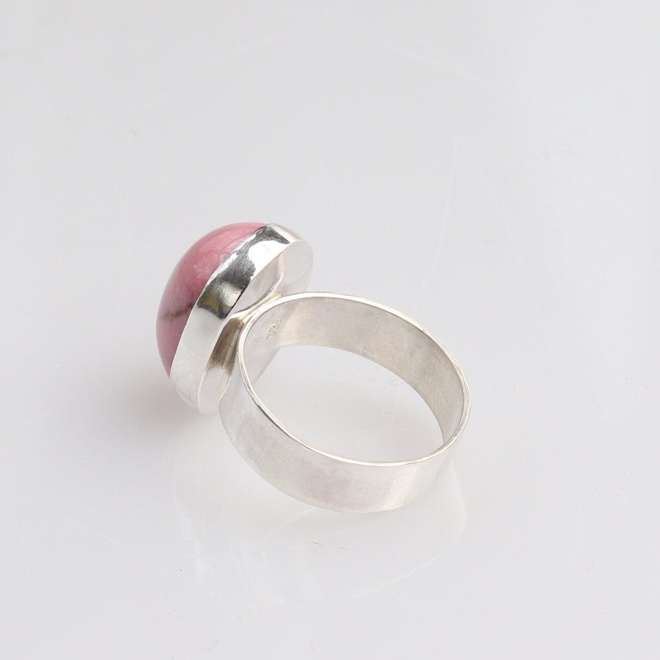 A back view of this handcrafted oval pink Rhodonite gemstone ring is a true one-of-a-kind treasure. The stone has been handcut and polished into a smooth cabochon to reveal its rich rose hue and subtle black veining.