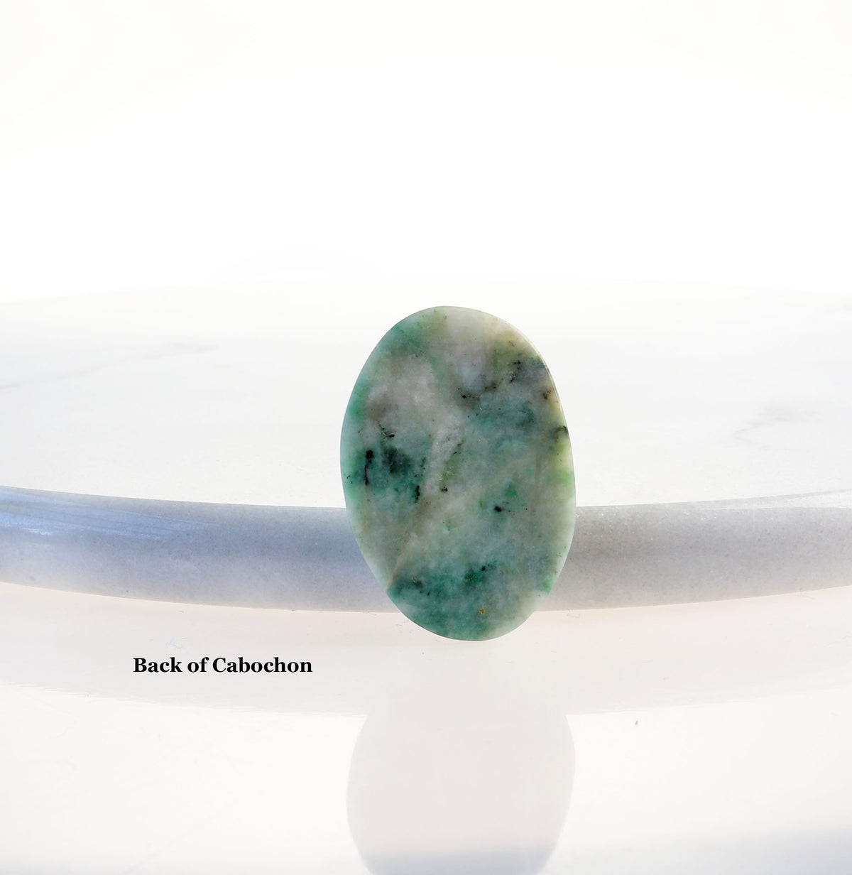 The back view of this African Turquoise Jasper oval cabochon gemstone with a marbled pattern of blue-green, teal, cream and black tones, shown from the back resting on a white surface with a text label 'Back of Cabochon'.