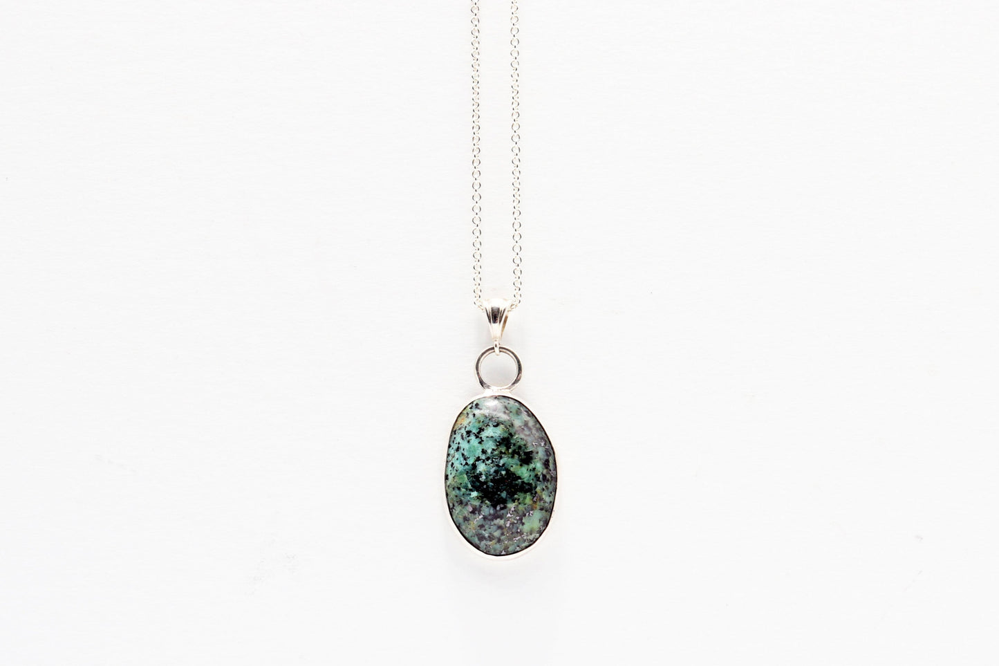 Fraser River Turquoise featuring blue green and black patterns showcased in Argentium Silver and fine silver setting. pendant on a white background