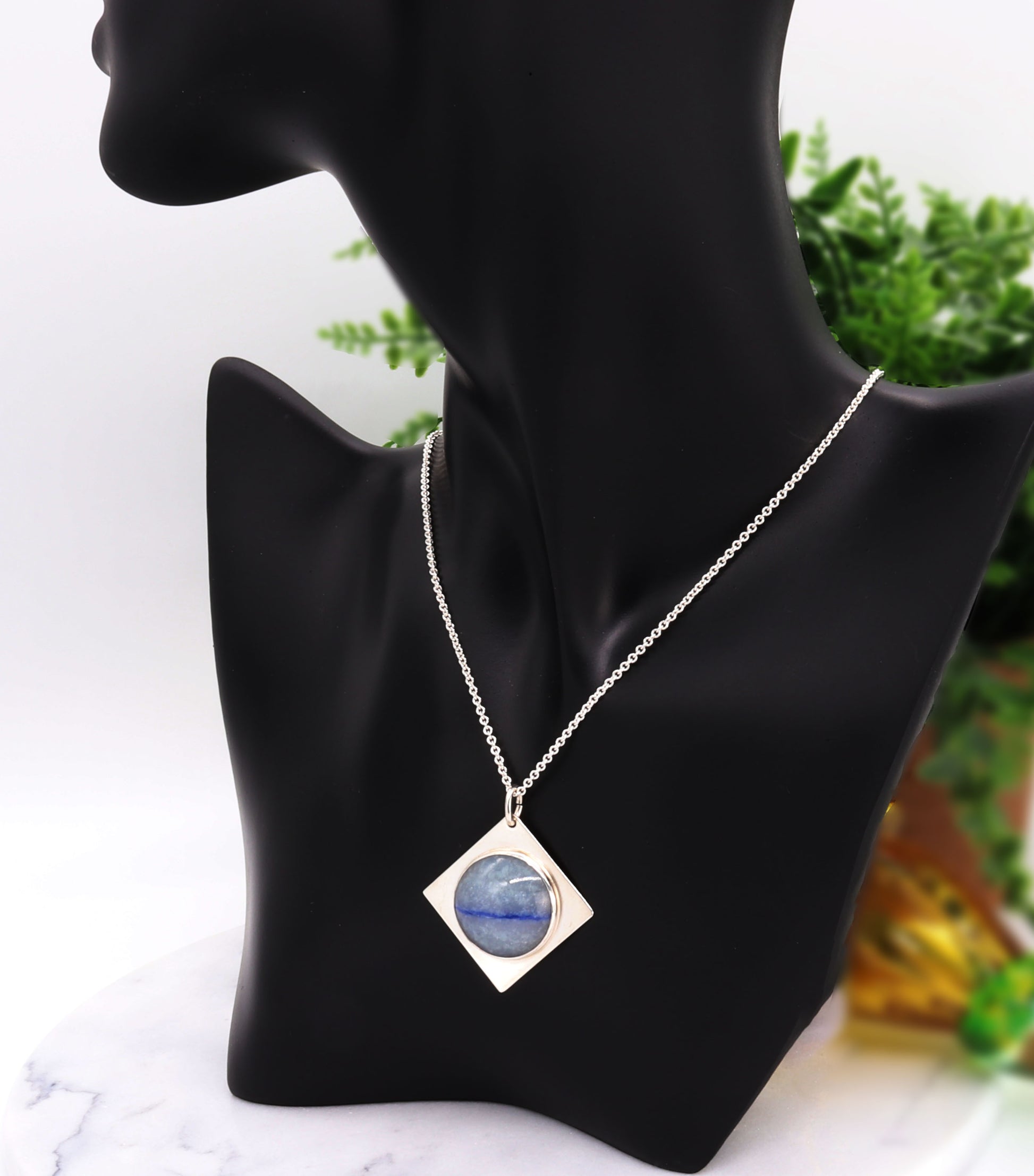 A handcut Blue Aventurine cabochon with shimmering crystalline structure and a deep indigo inclusion, reminiscent of Saturn’s rings.  Shown on black resin jewelry mannequin form with Argentium silver necklace attached.