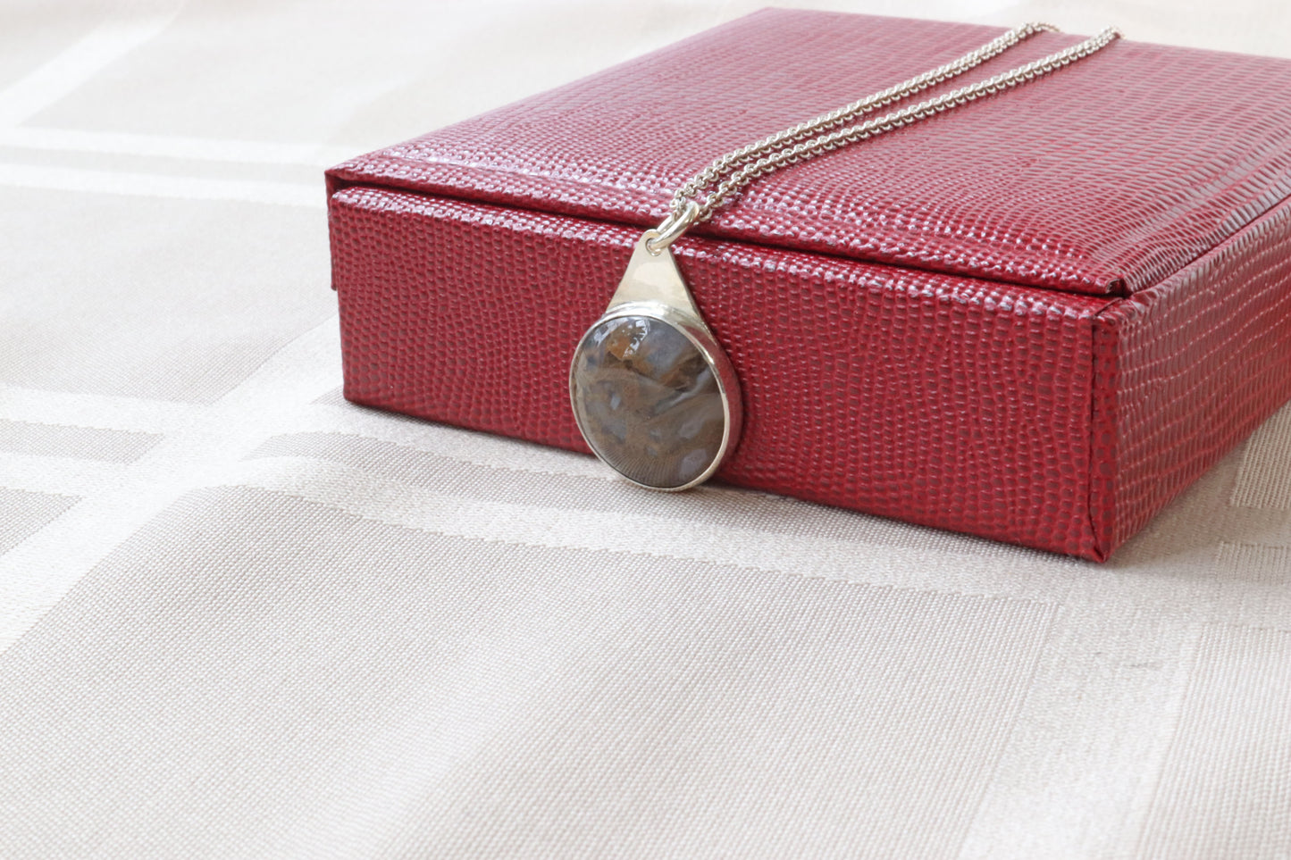 A 1 inch Rutilated Quartz gemstone with brown and golden-colored needle-like inclusions artistry. The gemstone is encased in a meticulously crafted Argentium® 935 Silver; an ideal complement to any personal collection. Ready to gift in red faux leather gift box.