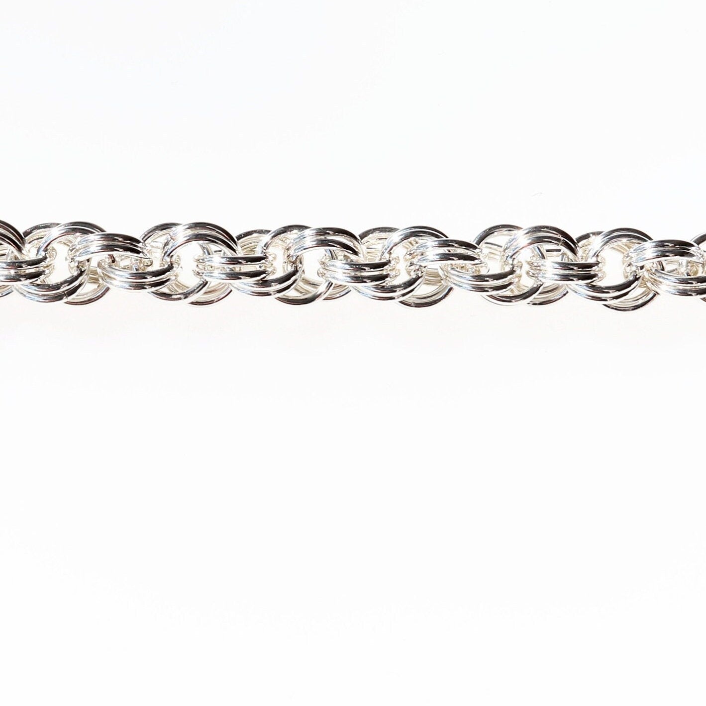 A close-up of the double-ring spiral weave of the Silver Spiral Bracelet. Crafted right in our Missouri studio and showcases the finest 935 Argentium® Silver. It features a unique design comprised of two rings for each link, with each spiral link consisting of a pair of interconnected rings. A custom hammered S hook clasp ensures easy on and hassle-free wearing.