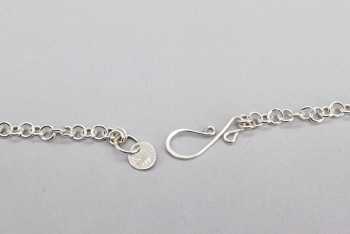 Close-up of an Argentium silver s-hook clasp with hallmark tag on a light gray background.