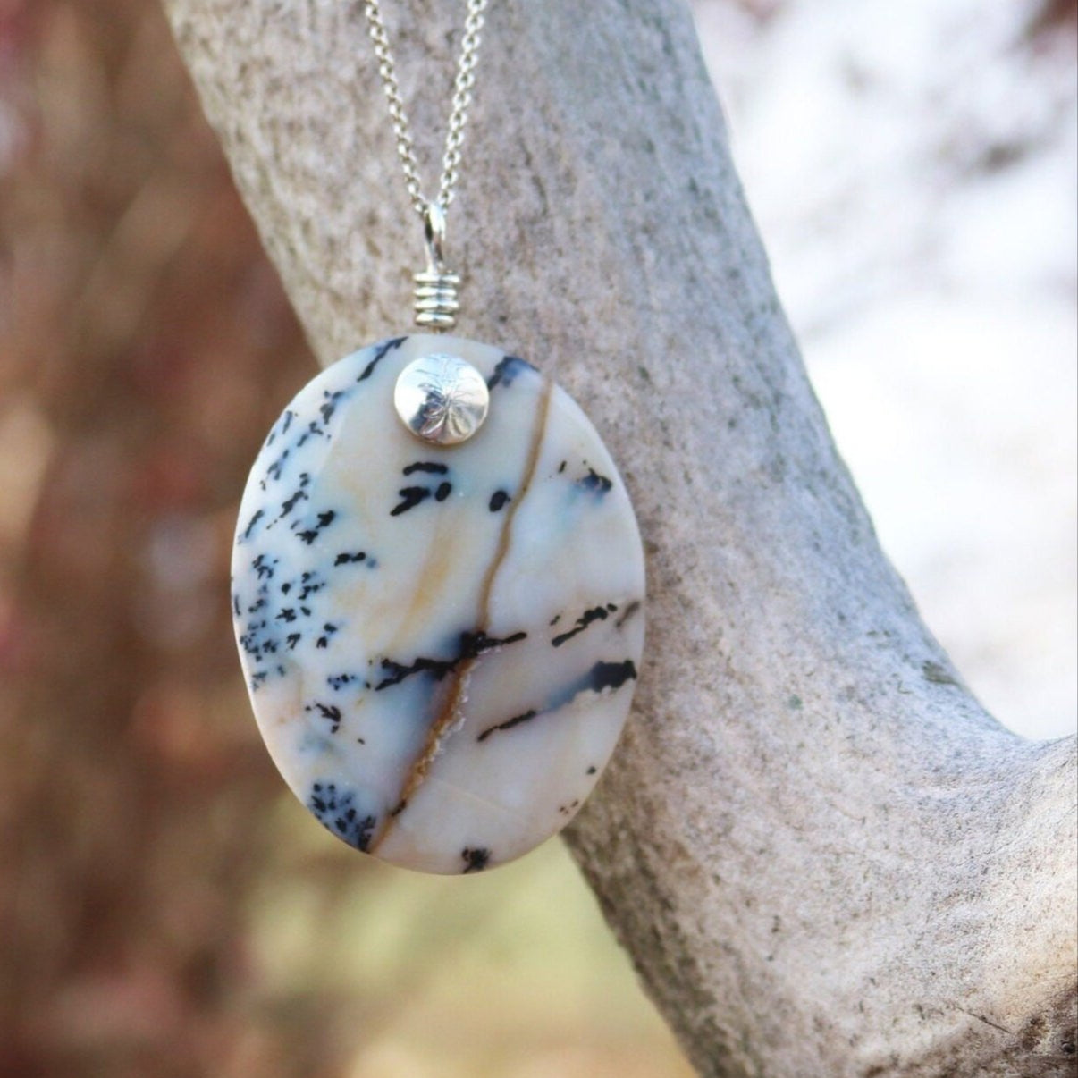 A truly magnificent 2.62 inch Dendritic Agate pendant, meticulously handcut and polished in our USA studio. Shown against elk branch outdoor background. This exceptional cabochon pendant showcases striking black branching inclusions set against a background that transitions from opaque to partially translucent.