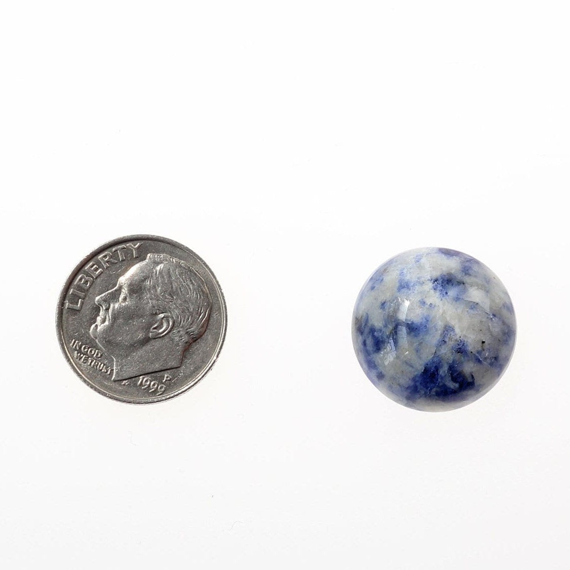 Close-up view of a  Natural Blue Brazilian Sodalite oval cabochon. This stunning variety of Sodalite has been handcut and polished to reveal the reveal the striking blue and white hues and captivating pattens that will surely stand out in your crafts. A US dime is shown for size comparison; the coin displays the text 'LIBERTY' and 'IN GOD WE TRUST', along with the year '1999'.