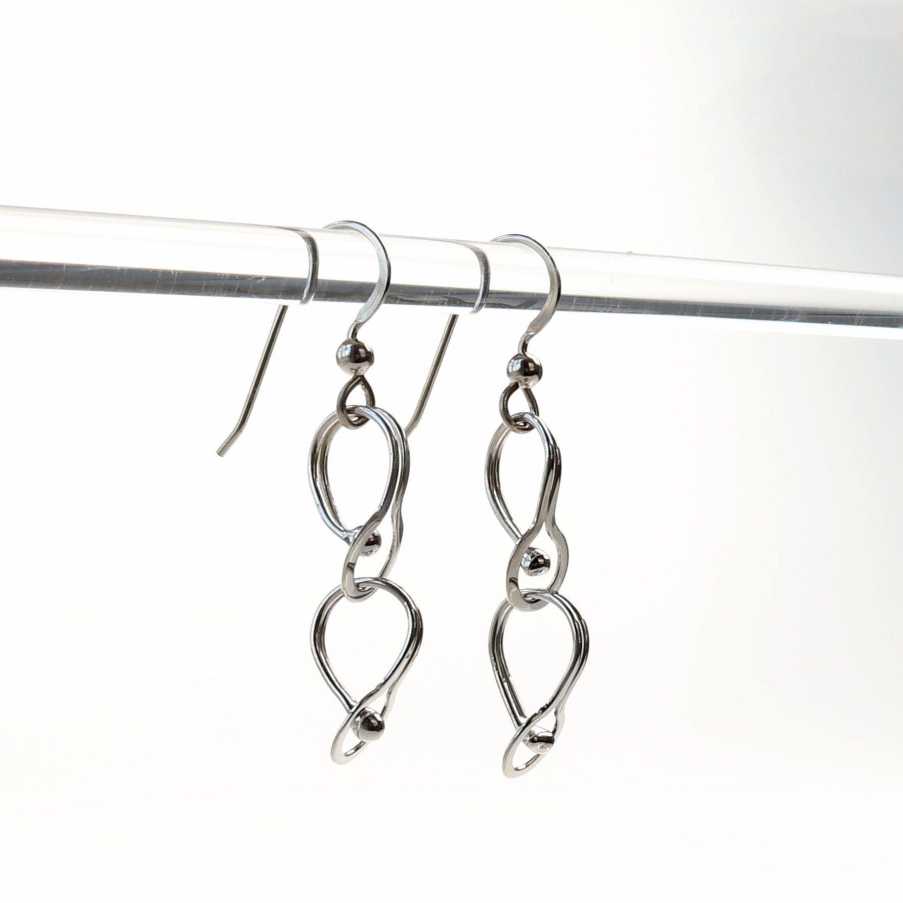 Double loop dangle earrings handcrafted in Argentium® 940 silver, featuring two twisted open loops linked vertically. Displayed hanging from a clear rod.