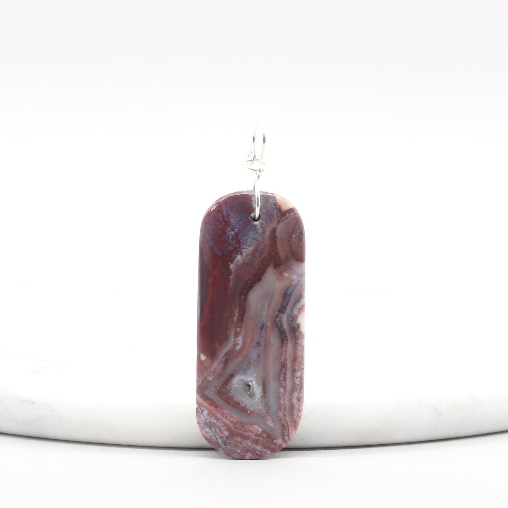 Front view of Red Mexico Agate pendant featuring soft lavender and mauve tones, polished to highlight translucent patterns, with a silver infinity-style bail.  Shown against white marble background.