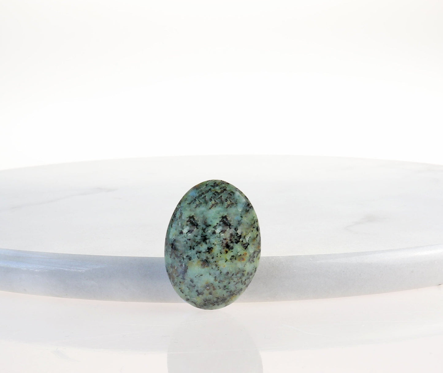 Oval Fraser River Turquoise Cab shown against a white marble background.