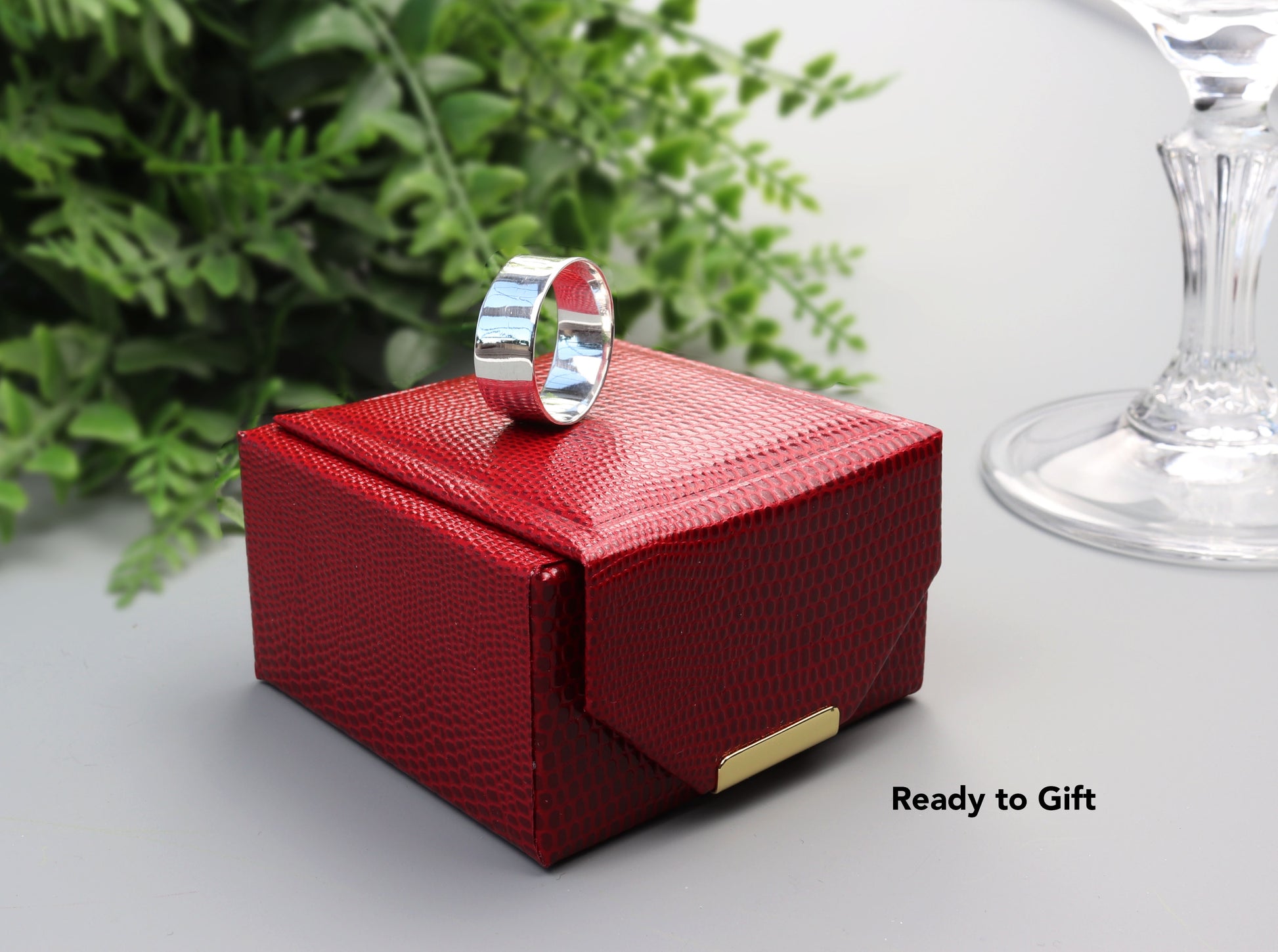 A closeup of our Argentium® 935 silver band that features a subtle anticlastic curve—gently contoured to enhance both comfort and style. Shown on the top of a stylish red faux leather gift box that is included in purchase and ready for gifting or storage.