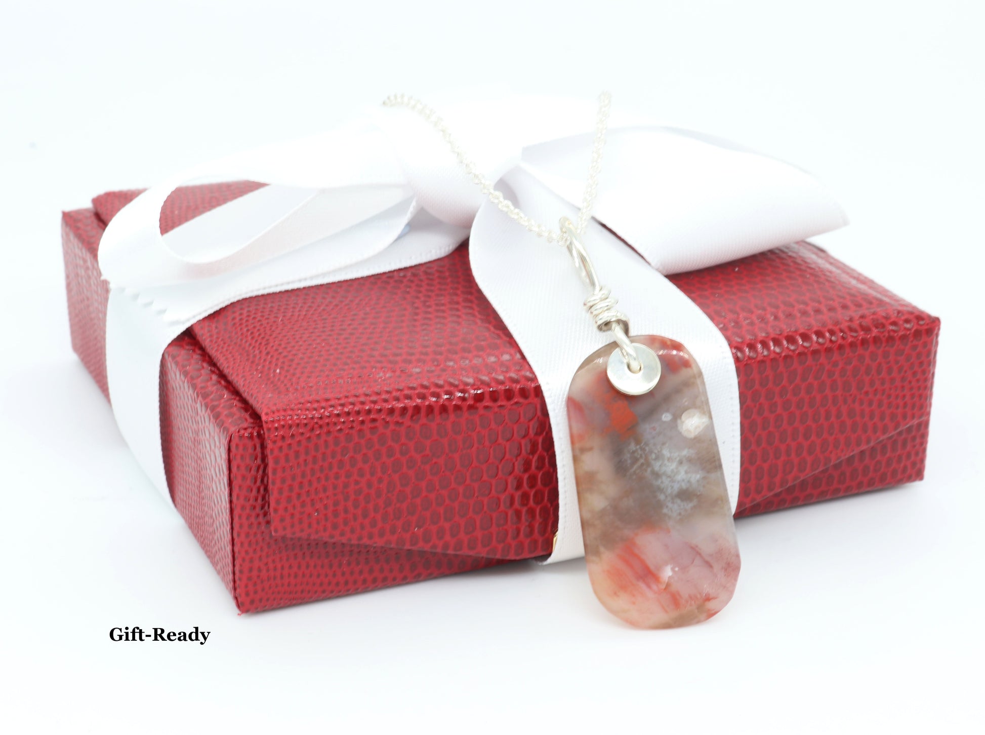 Gift Ready is this one-of-a-kind pendant featuring a stunning tag-shaped cabochon of Petrified Rainbow Wood, hand-cut and polished to reveal warm hues of red, mauve, white, and translucent veining.  Shown with red stylish gift box with white satin ribbon.