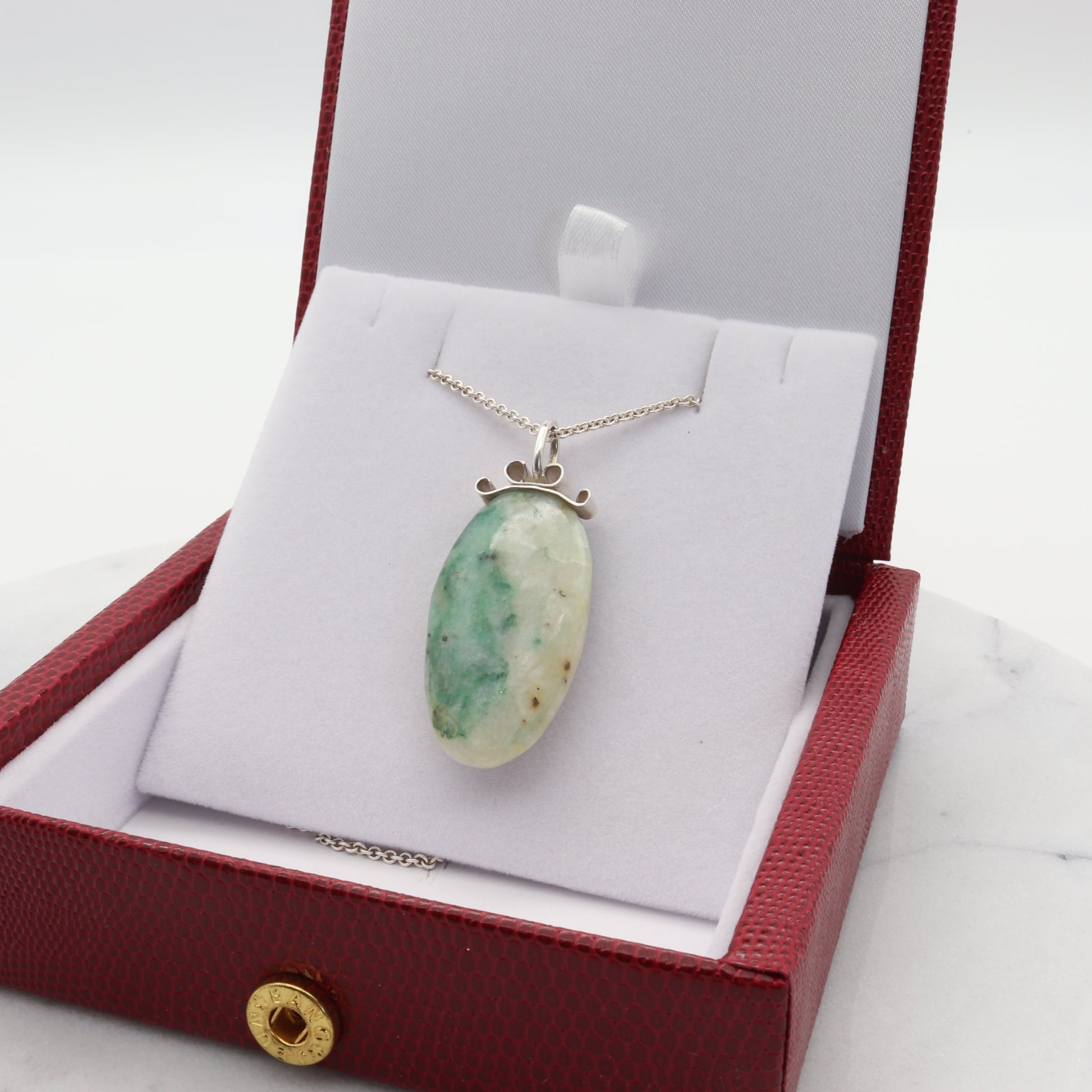 A stunning 1.81 inch natural African Turquoise Jasper reversible pendant. Handcut and freeform polished to reveal the unique shades of green and cream hues crafted with a premium bow-shaped wire bail in sterling 935 Argentium silver plus a complementary sterling 935 Argentium chain ensuring both style and longevity.  Ready to gift in a faux red leather gift box.