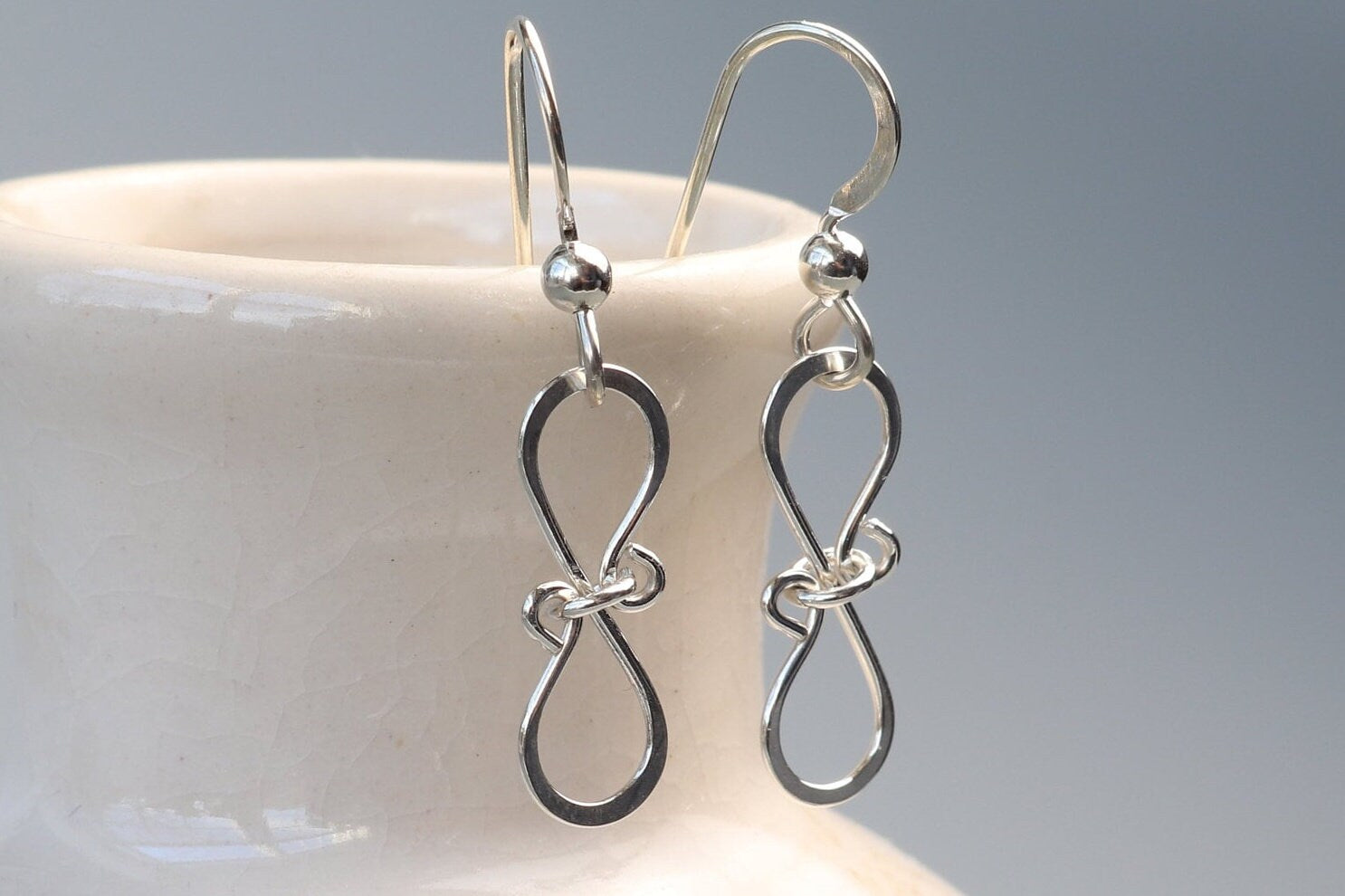 Introducing our exquisite handcrafted Infinity Bow Shaped Earrings, meticulously created in our USA Studio. These stunning earrings feature a beautiful hammered finish made with the finest quality sterling 935 Argentium silver, known for its hypoallergenic and tarnish-resistant properties. 
The earrings are designed with .032 inch ear wire to ensure a comfortable fit. 
Each pair comes carefully packaged in a charming gift box.