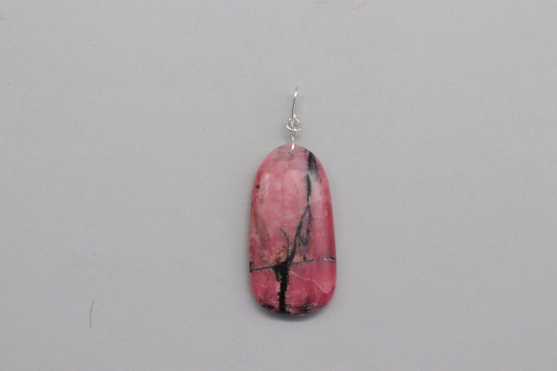 A polished Rhodonite pendant on both sides and features a handcrafted infinity bow-shaped bail made from hypoallergenic, tarnish-resistant Argentium® 935 silver.