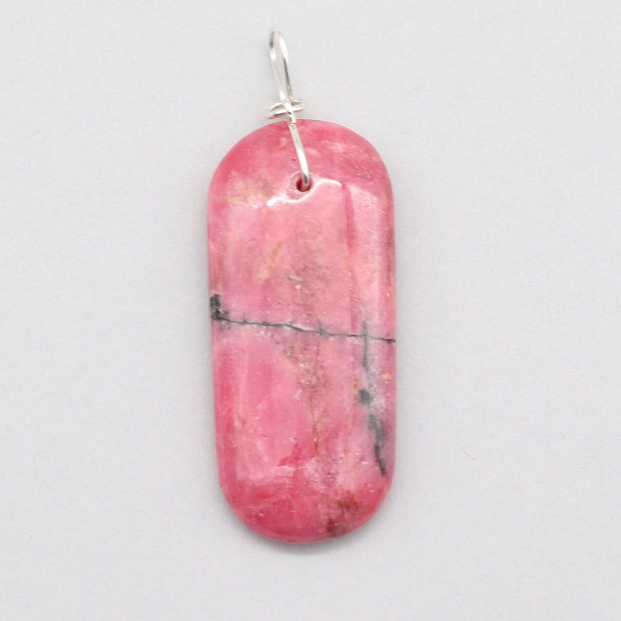 A natural Rhodonite crystal pendant in candy pink with black inclusions, sourced from our personal collection. This gemstone has been handcut and polished in our Missouri studio to highlight its natural beauty and crafted with an infinity shaped bow bail, in sterling Argentium 935 silver. To complete the look a complementary 935 Argentium silver chain is included.
