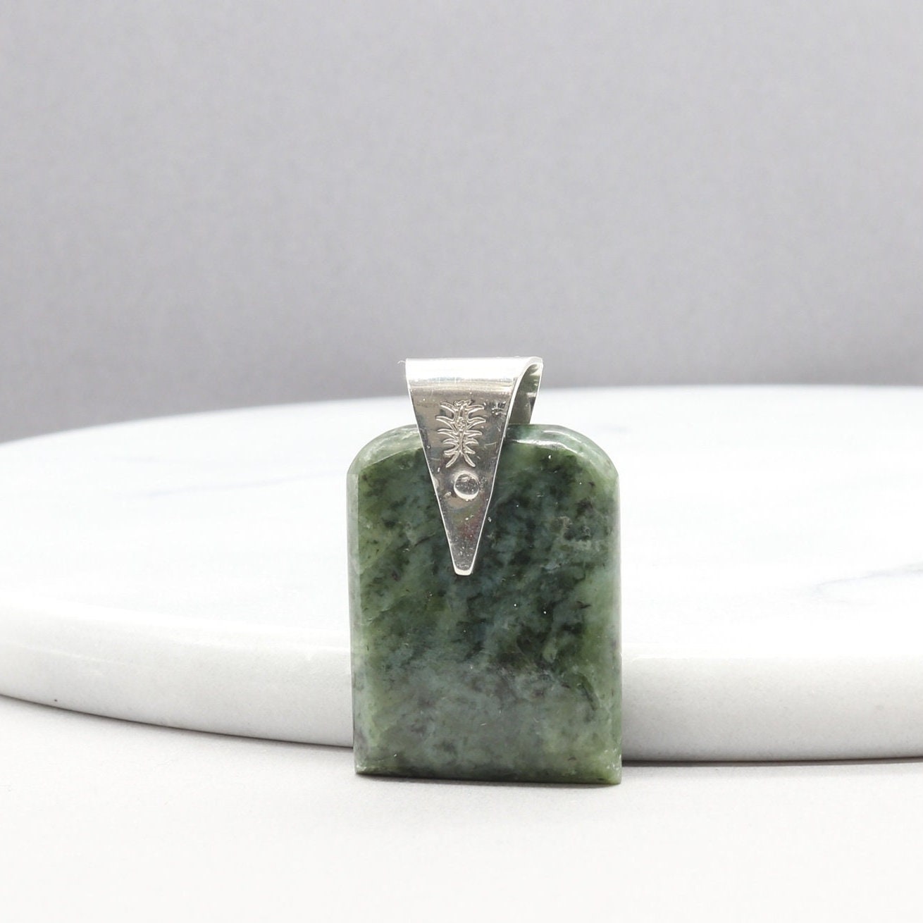 A Wyoming (Nephrite) Jade that I shaped and polished to bring out the light to dark sage translucent colors and patterns, into a distinctive tombstone tag shape. The custom-crafted bail with the Elkhorn Silver™ Crest makers mark, is sculpted from tarnish resistant and hypoallergenic sterling Argentium® 935 Silver.