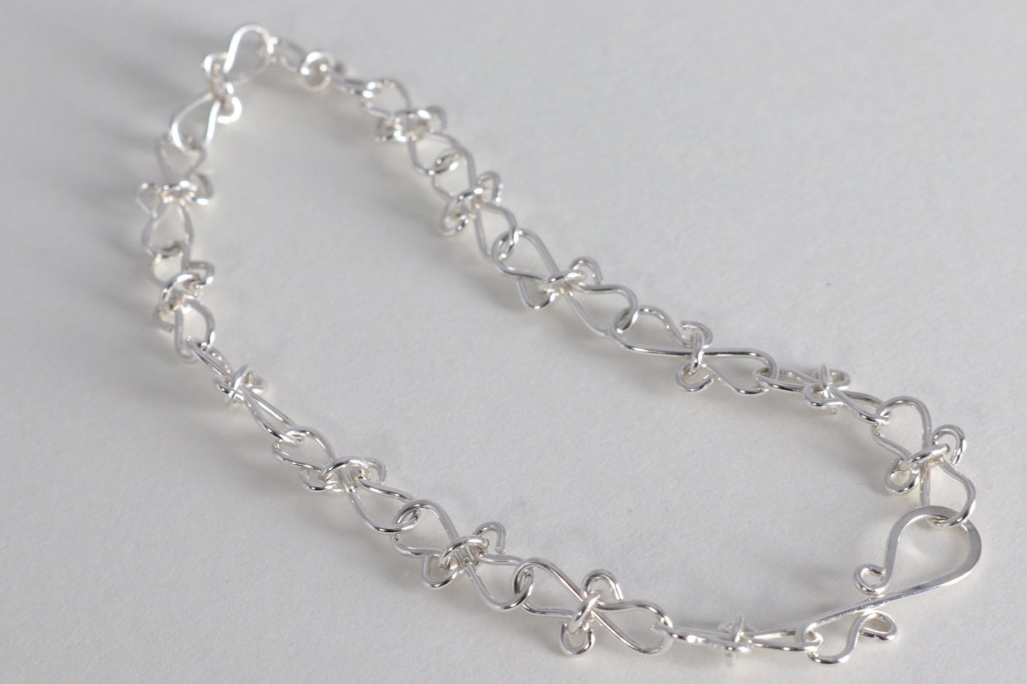 Infinity bow shaped chain bracelet handcrafted from solid sterling 935 Argentium Silver, ensuring its resistance to tarnish while being hypoallergenic for sensitive skin. The bracelet measures 7.5 in length, with an adjustable design that allows you to find the perfect fit by increments of half inch. A custom S hook clasp that enables easy wearing and removal.