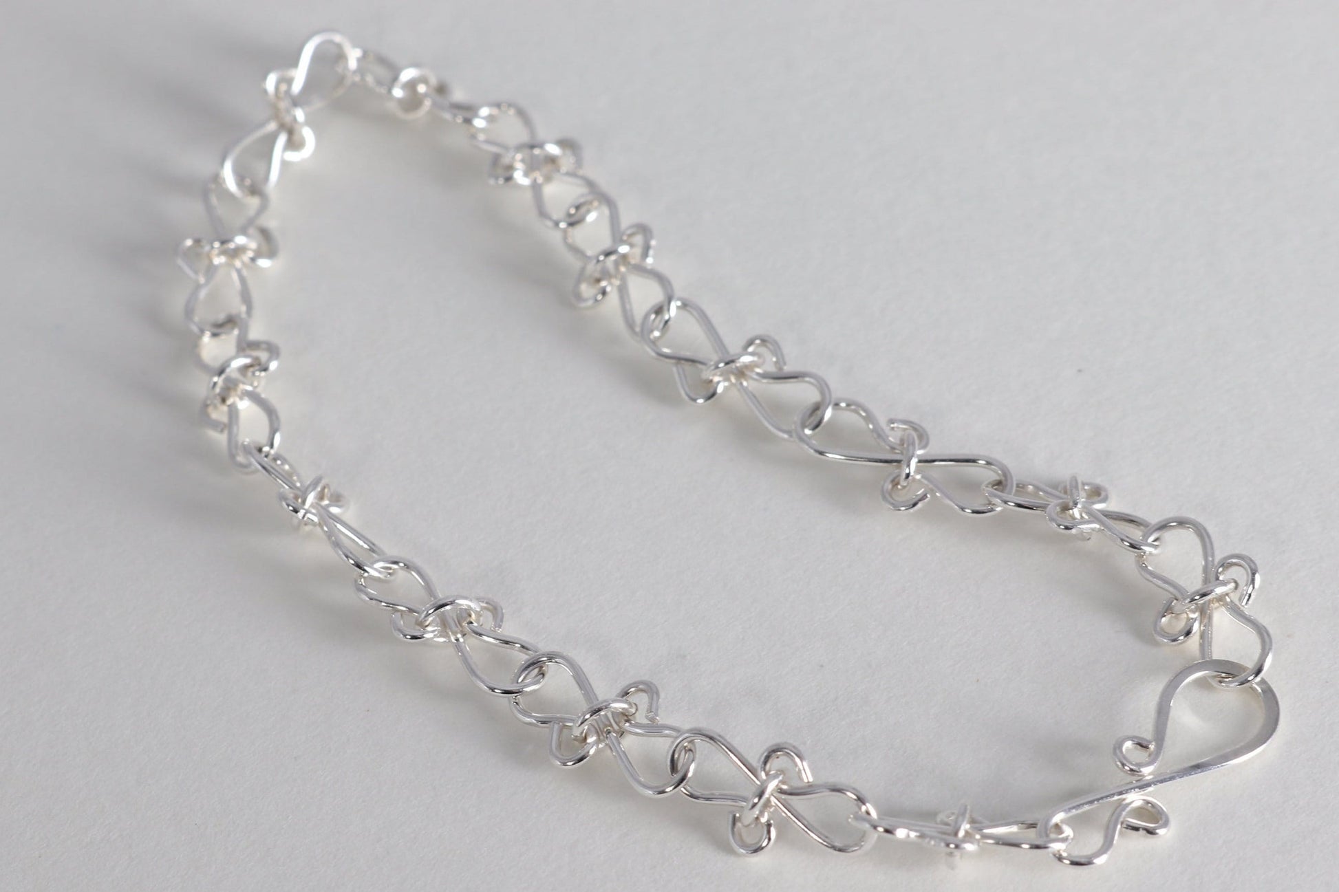 Infinity bow shaped chain bracelet handcrafted from solid sterling 935 Argentium Silver, ensuring its resistance to tarnish while being hypoallergenic for sensitive skin. The bracelet measures 7.5 in length, with an adjustable design that allows you to find the perfect fit by increments of half inch. A custom S hook clasp that enables easy wearing and removal.
