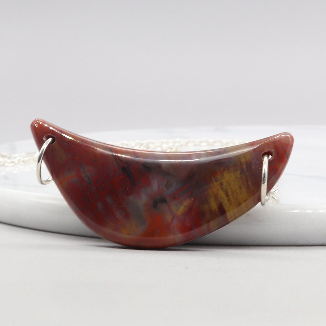 A piece of Arizona's history in this stunning sterling Petrified Rainbow Wood crescent moon pendant. Handcrafted with sterling Argentium® Silver 935 bow shaped dual wire bails and single cable chains. Handcut and polished into a moon shaped crescent to reveal the remarkable translucent colors and patterns of nature's artistry on both sides of the pendant.