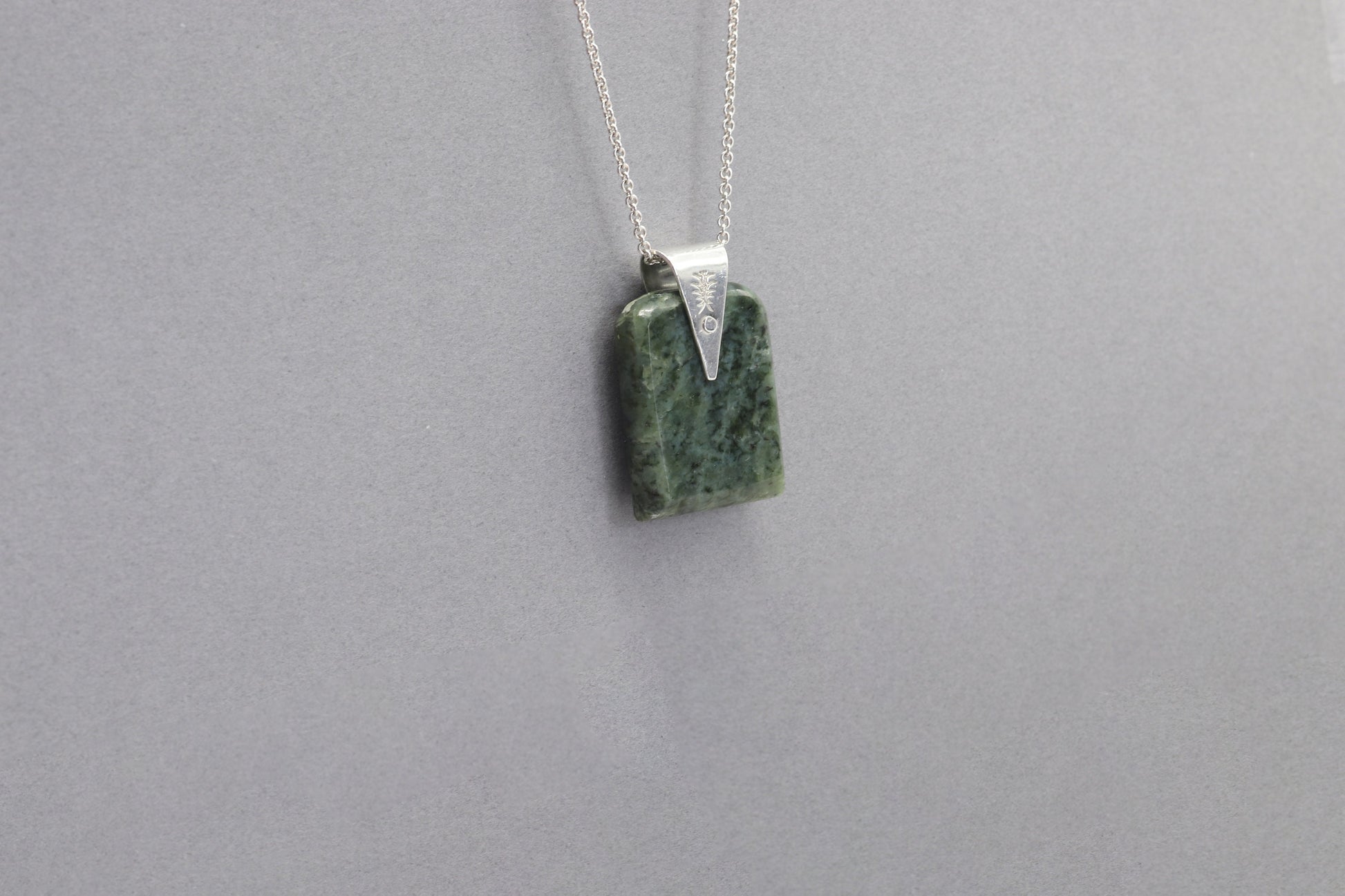 A Wyoming (Nephrite) Jade that I shaped and polished to bring out the light to dark sage translucent colors and patterns, into a distinctive tombstone tag shape. The custom-crafted bail with the Elkhorn Silver™ Crest makers mark, is sculpted from tarnish resistant and hypoallergenic sterling Argentium® 935 Silver.