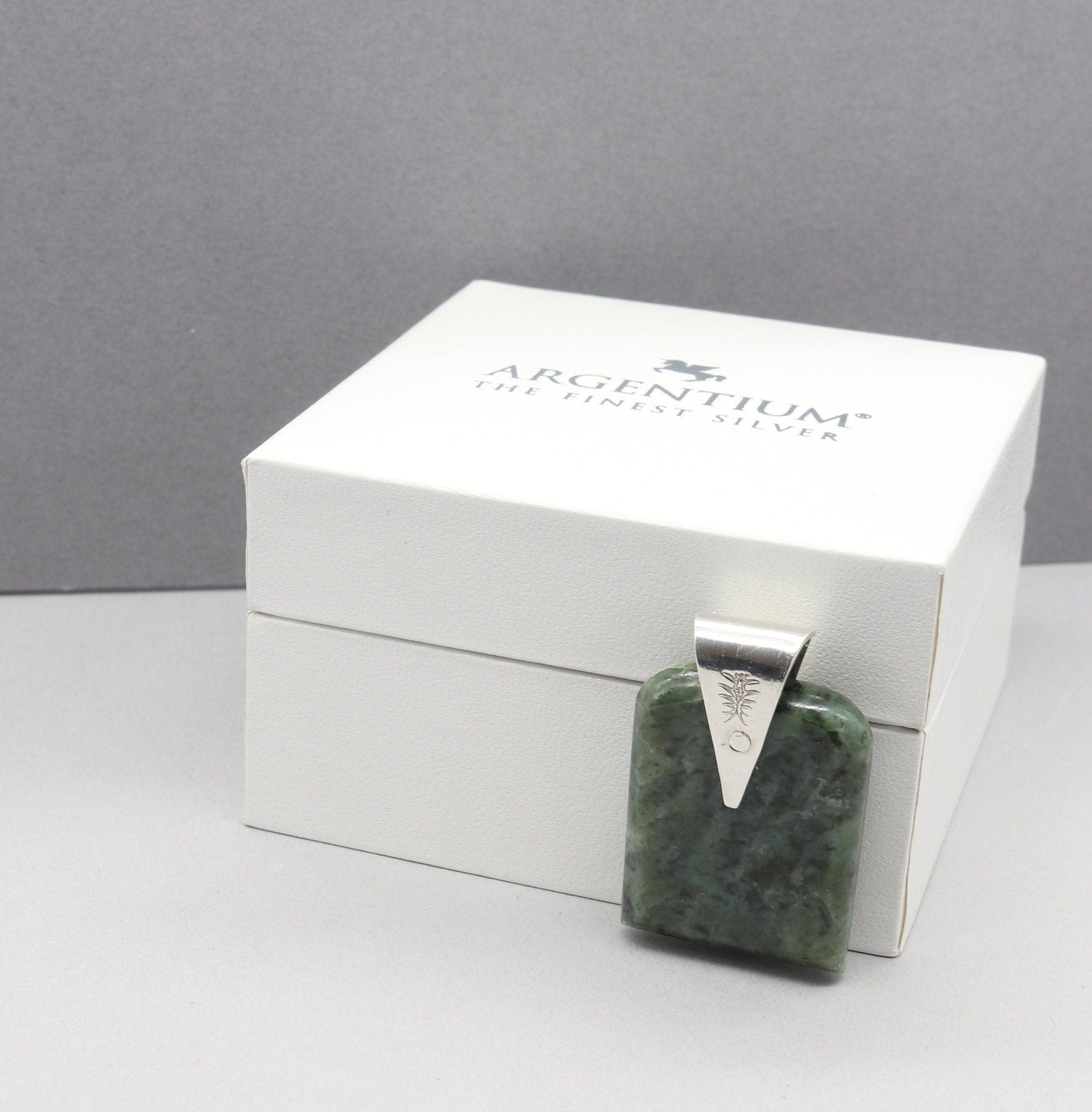 A Wyoming (Nephrite) Jade that I shaped and polished to bring out the light to dark sage translucent colors and patterns, into a distinctive tombstone tag shape. The custom-crafted bail with the Elkhorn Silver™ Crest makers mark, is sculpted from tarnish resistant and hypoallergenic sterling Argentium® 935 Silver.  Ready to gift in a stylish gift box.